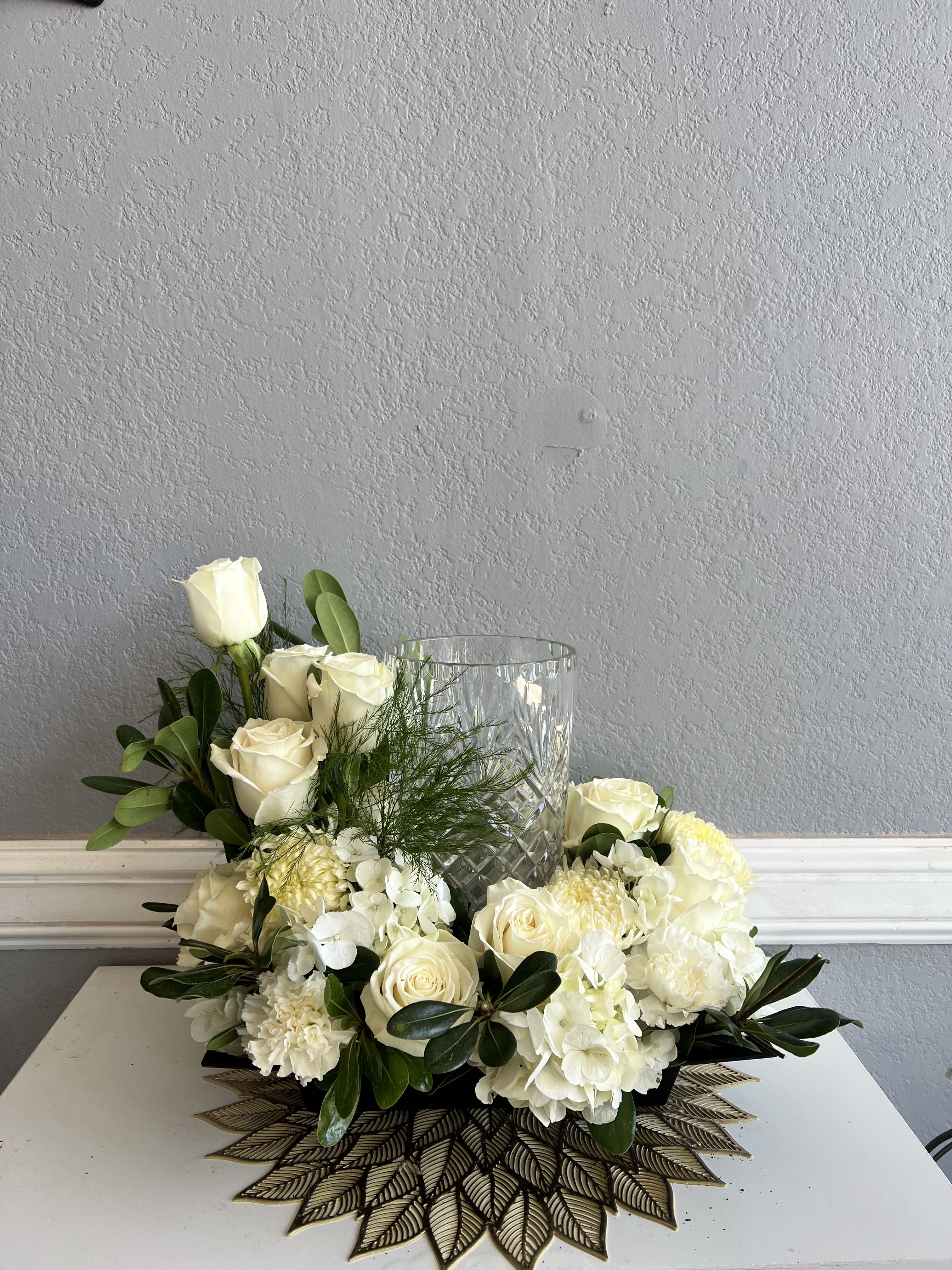 White roses and hydrangeas arranged around a clear glass vase