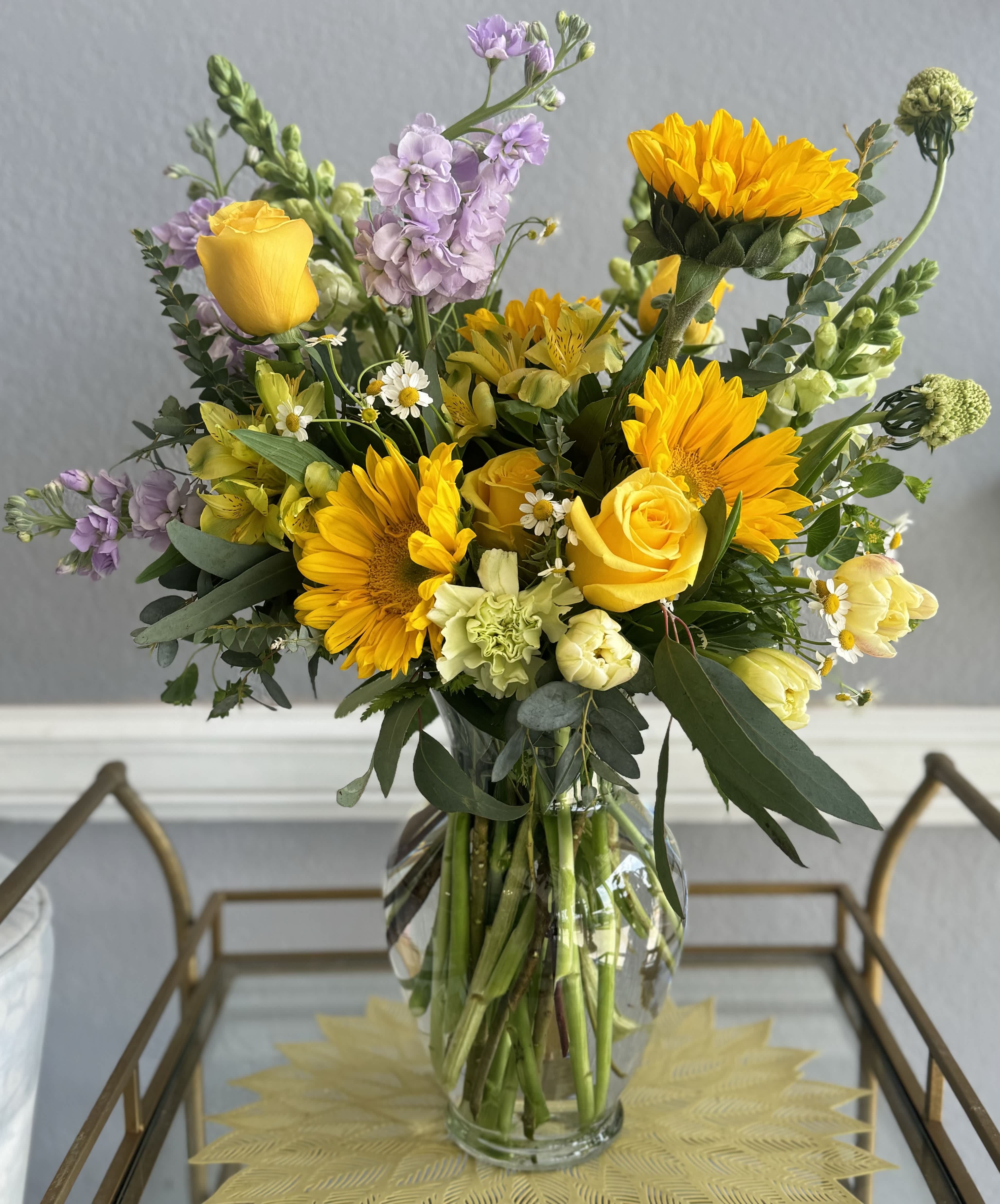Bouquet of yellow roses, sunflowers, and lavender flowers in a glass vase