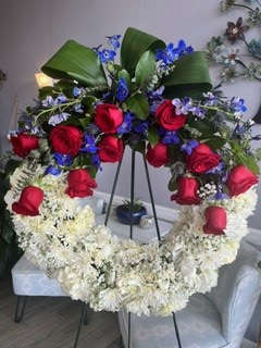 Standing floral wreath with red roses and white flowers on a black easel