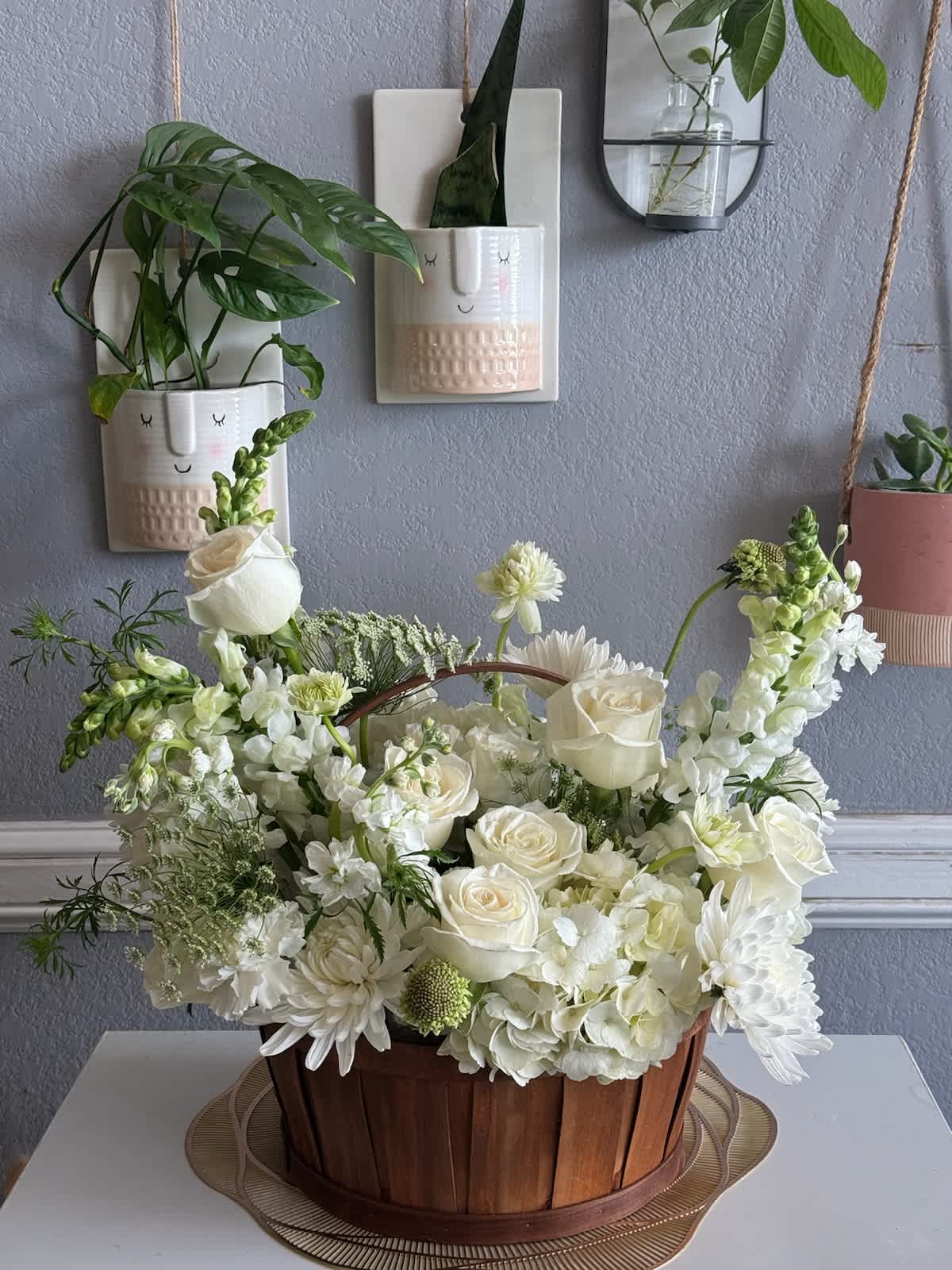 White floral arrangement in a wooden basket with roses and daisies