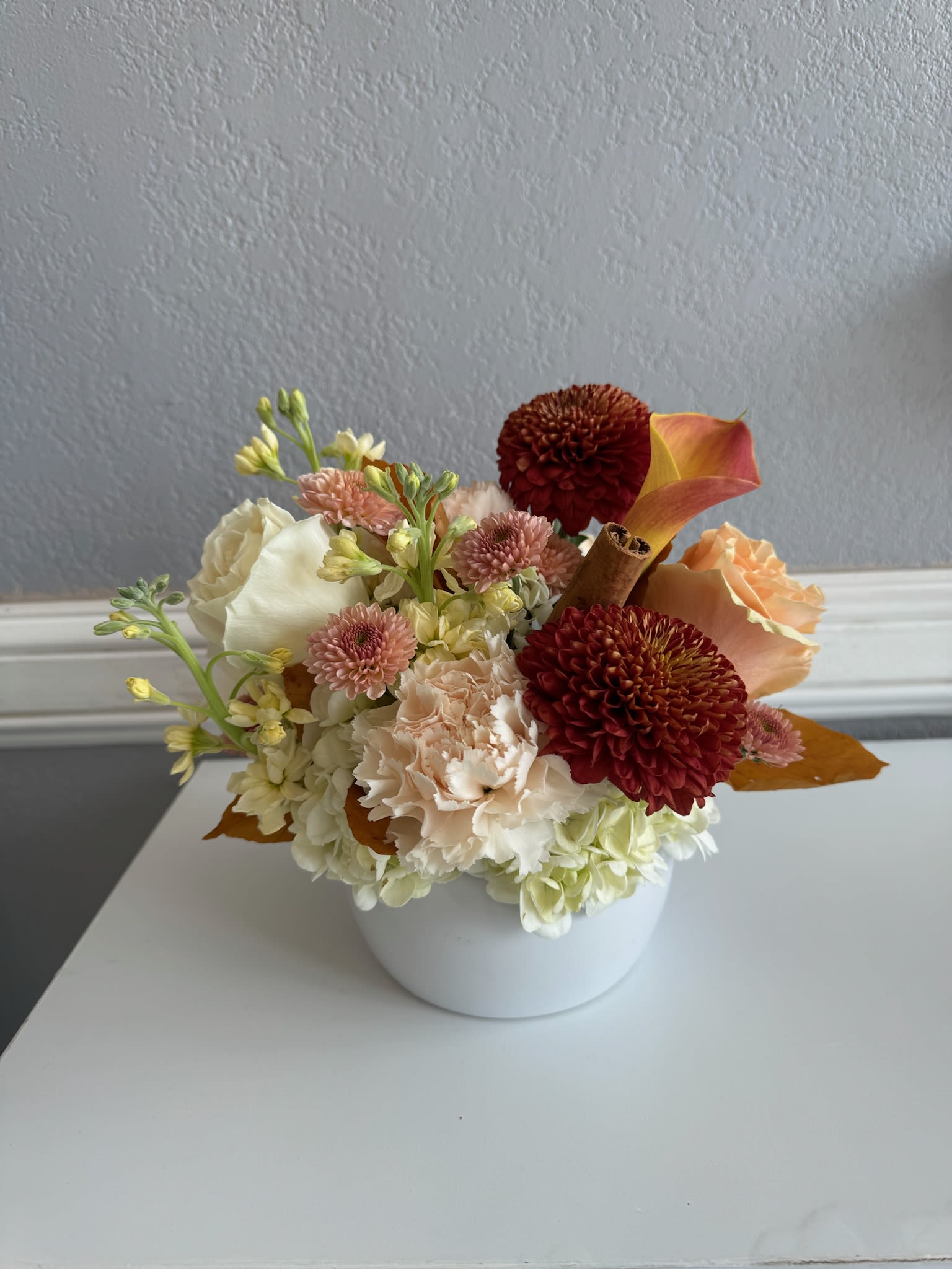 Compact floral arrangement in a white bowl vase with cream, peach, and burgundy blooms