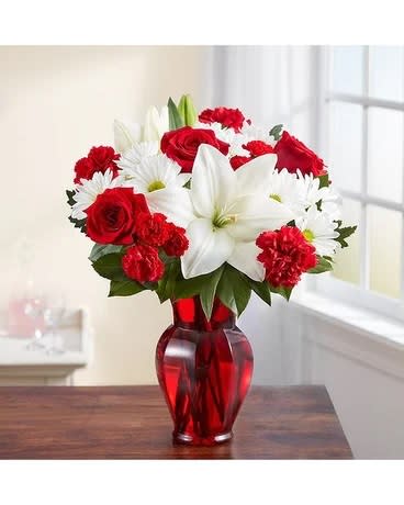 Red roses, white lilies, and white daisies in a red glass vase