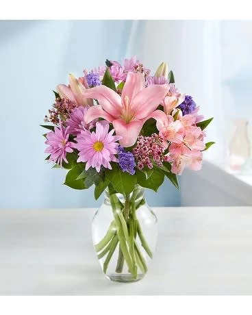 Pink lilies and purple daisies in a clear glass vase