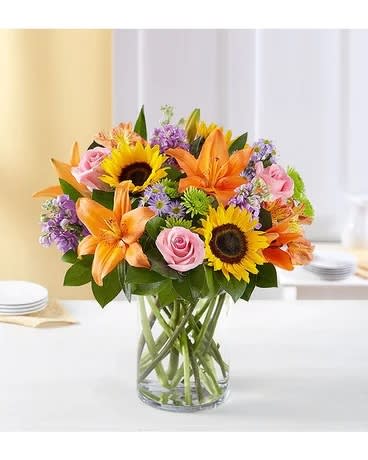 Mixed bouquet of sunflowers, lilies, and pink roses in a glass vase