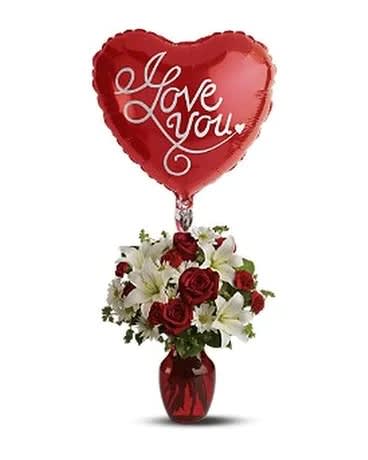 Heart-shaped red balloon above a vase of red roses and white lilies