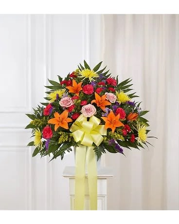 Colorful standing floral spray with lilies, roses, and a yellow ribbon