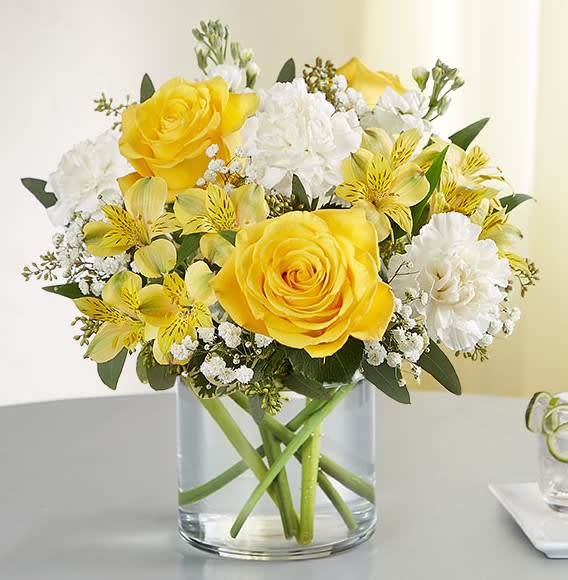 Yellow roses and white flowers arranged in a clear glass vase