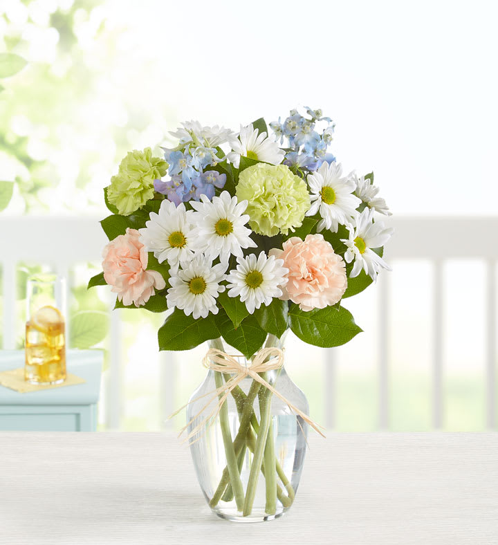 Bouquet of white daisies, pale carnations, and blue flowers in a glass vase