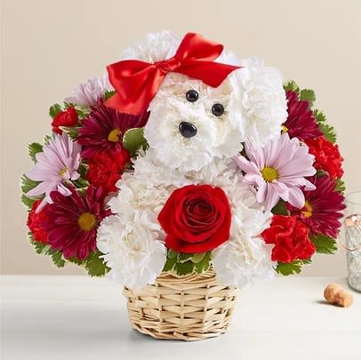 Flower arrangement shaped like a white dog with a red bow and rose in a wicker basket