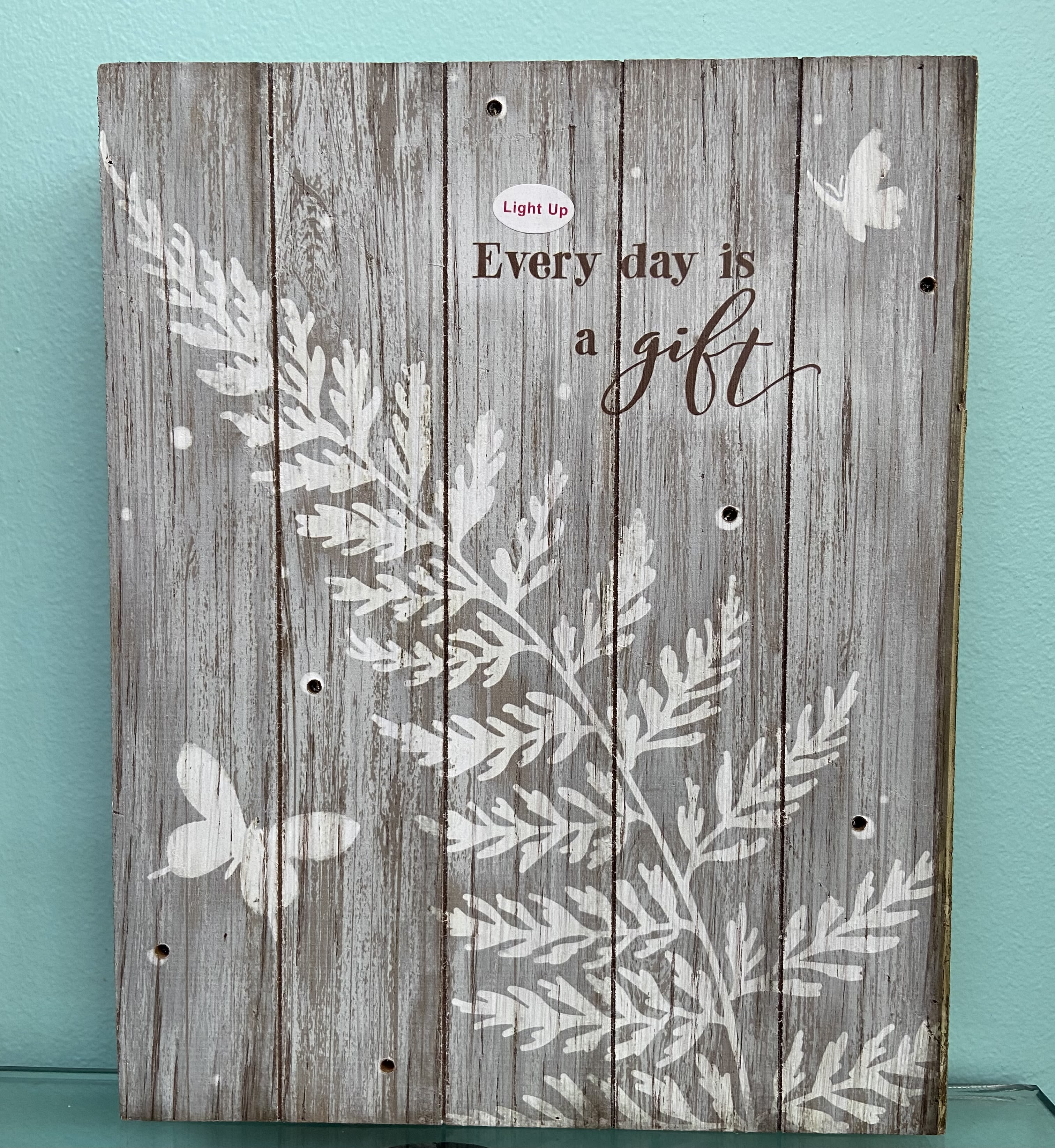 Rustic gray wooden sign with white foliage, butterflies, and the words "Every day is a gift".