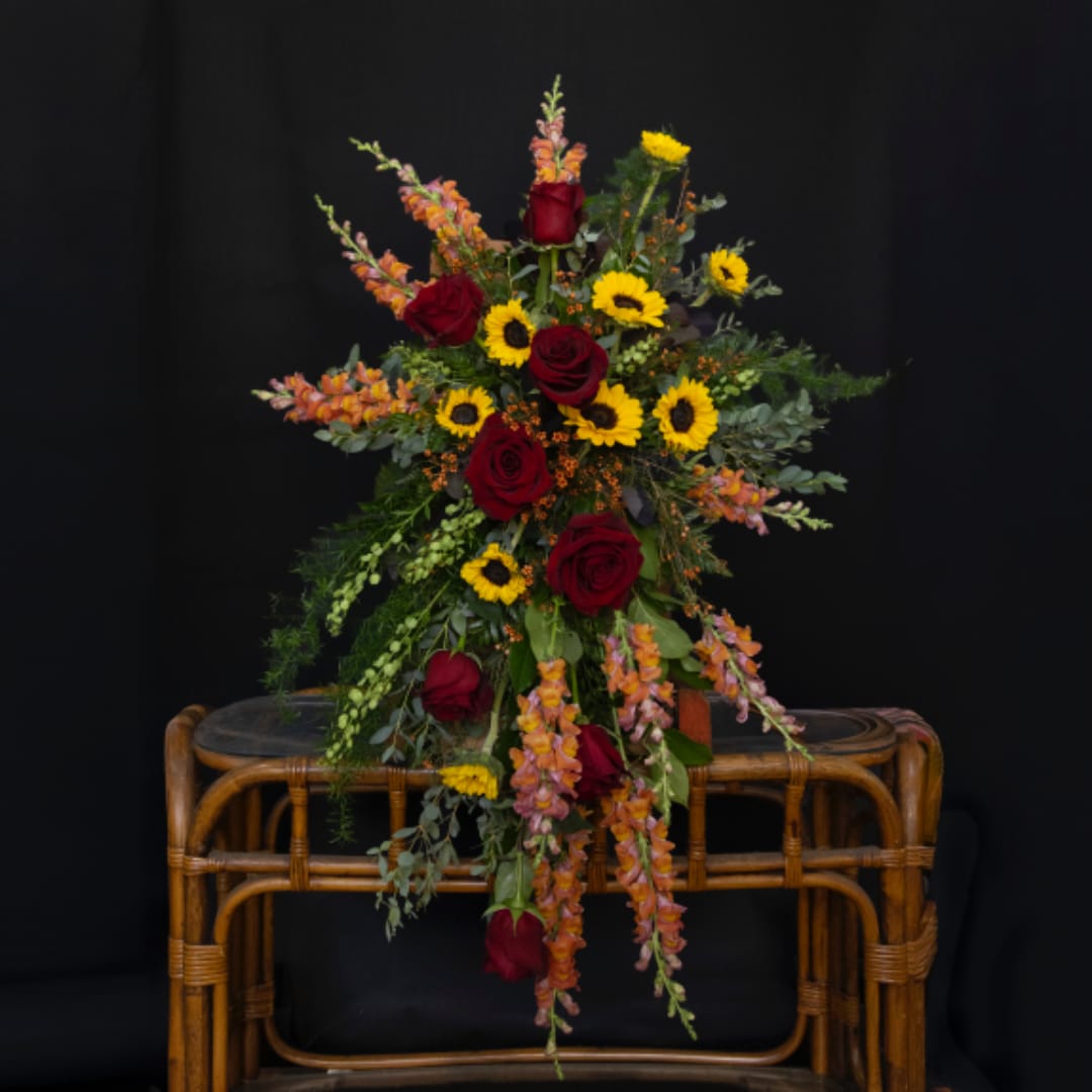 Tall arrangement of red roses and yellow sunflowers in a wicker stand