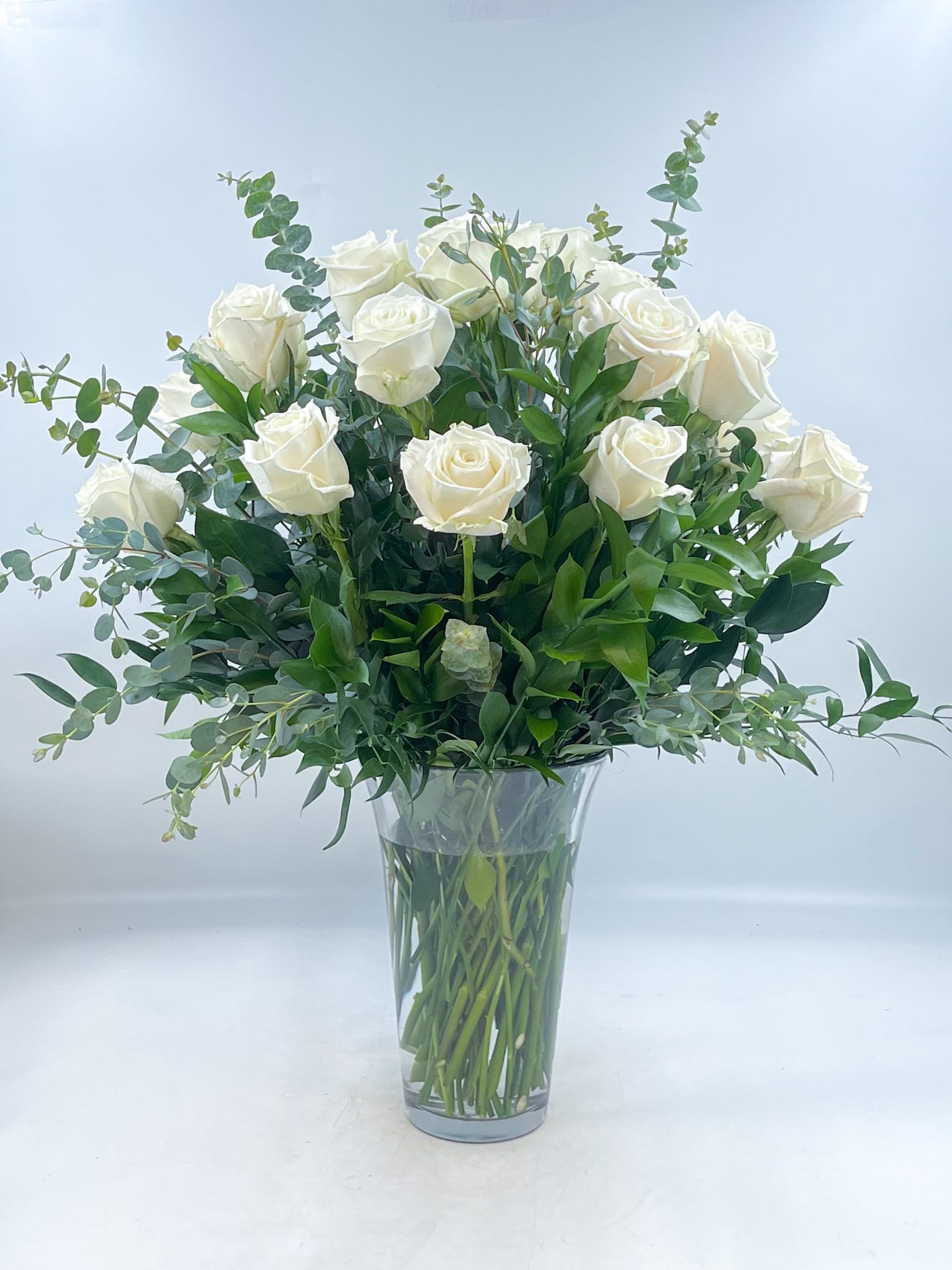 White roses arranged in a clear glass vase with greenery