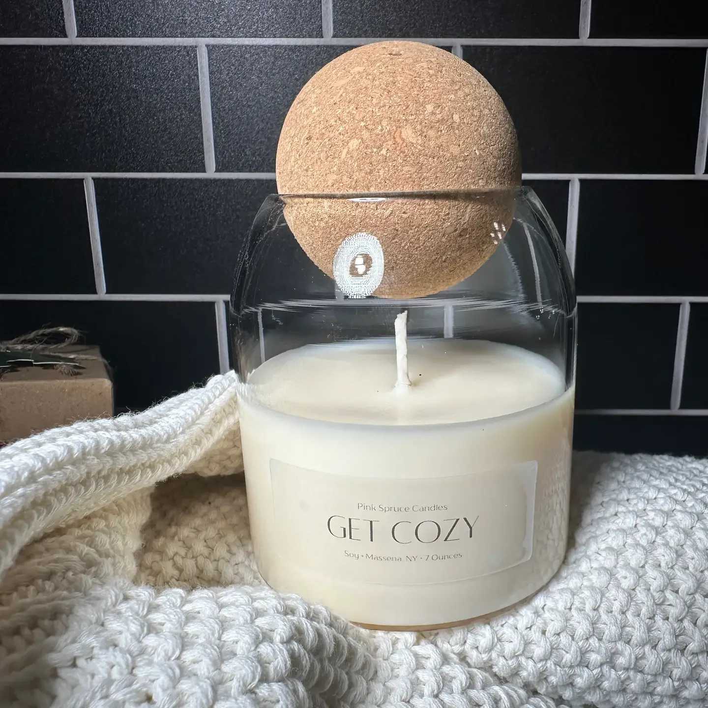 White candle in a glass jar with a cork lid and knitted wrap