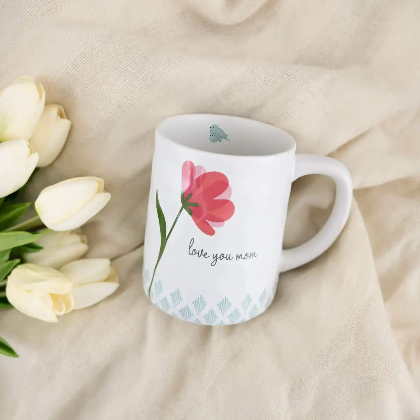 White mug with a pink flower graphic and "love you mom" text beside white tulips