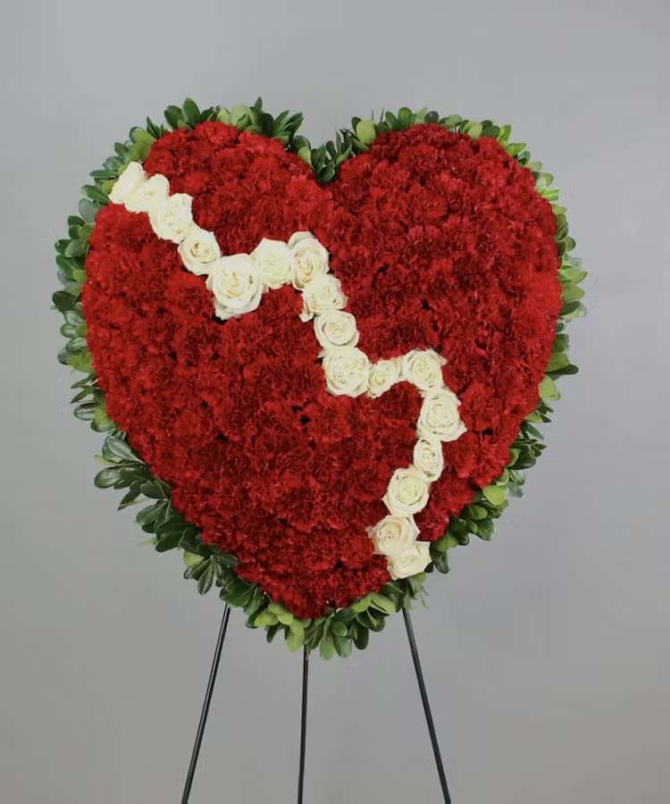 Heart-shaped red floral wreath with white roses on a stand