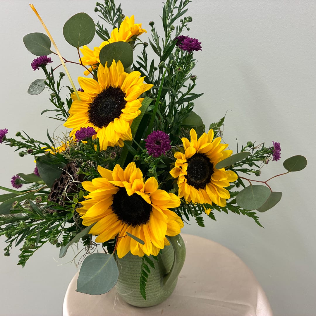 Sunflower arrangement with purple accent flowers in a green ceramic vase