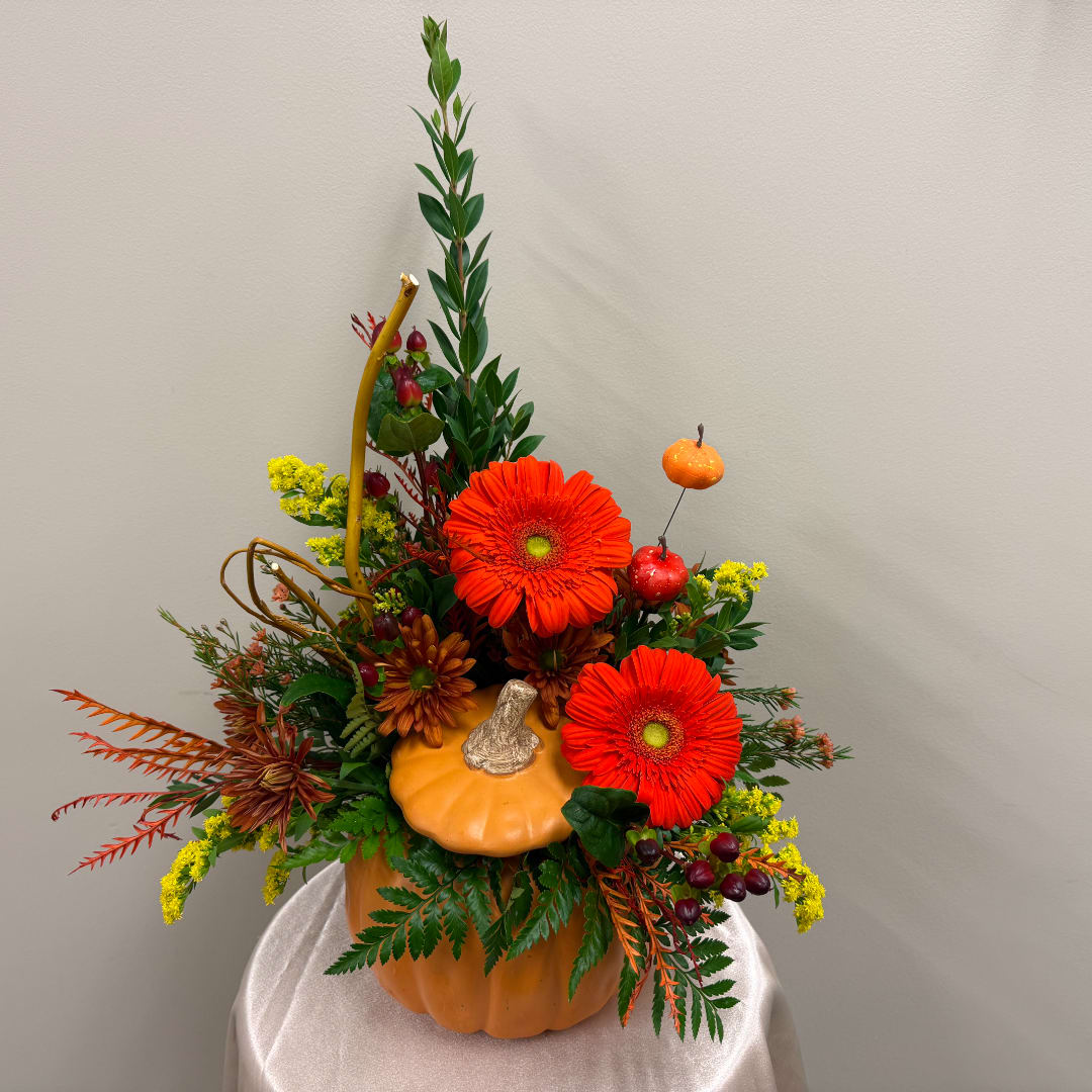 Autumn floral arrangement in a pumpkin container with orange gerberas and yellow accents