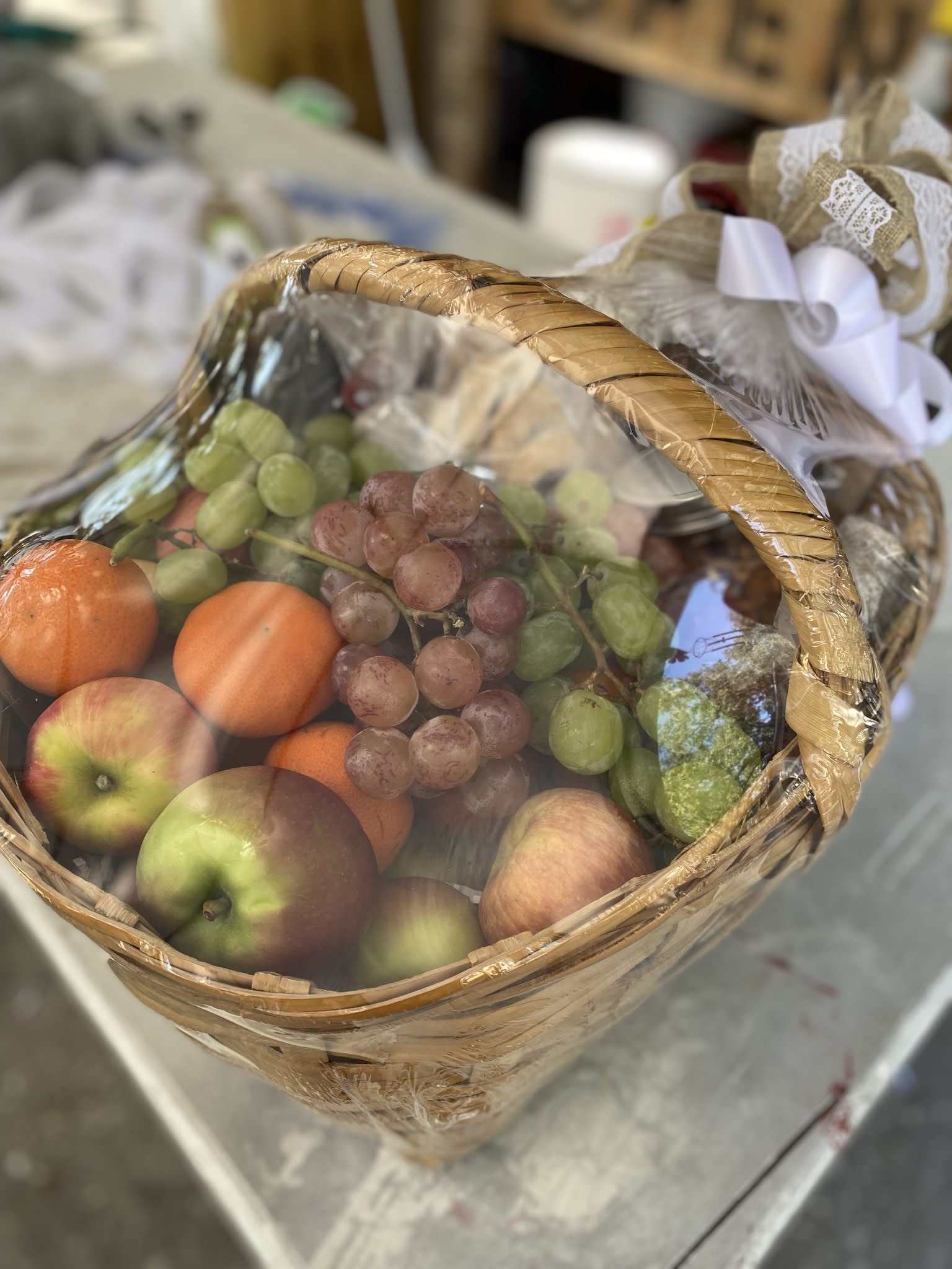 Gift basket of apples, oranges, and grapes wrapped in cellophane with a decorative bow