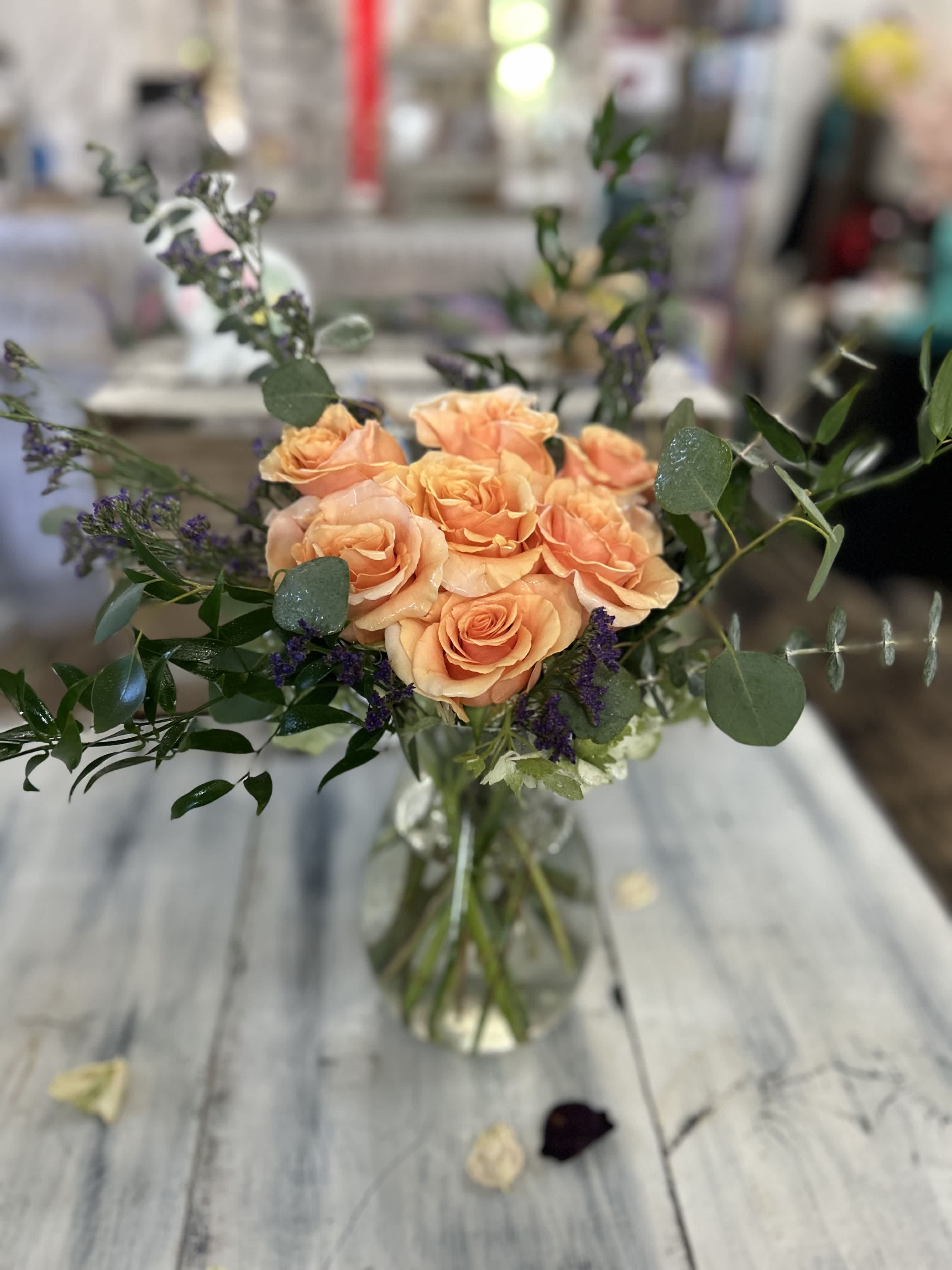 Peach rose arrangement with purple filler in a clear glass vase on a rustic wooden table