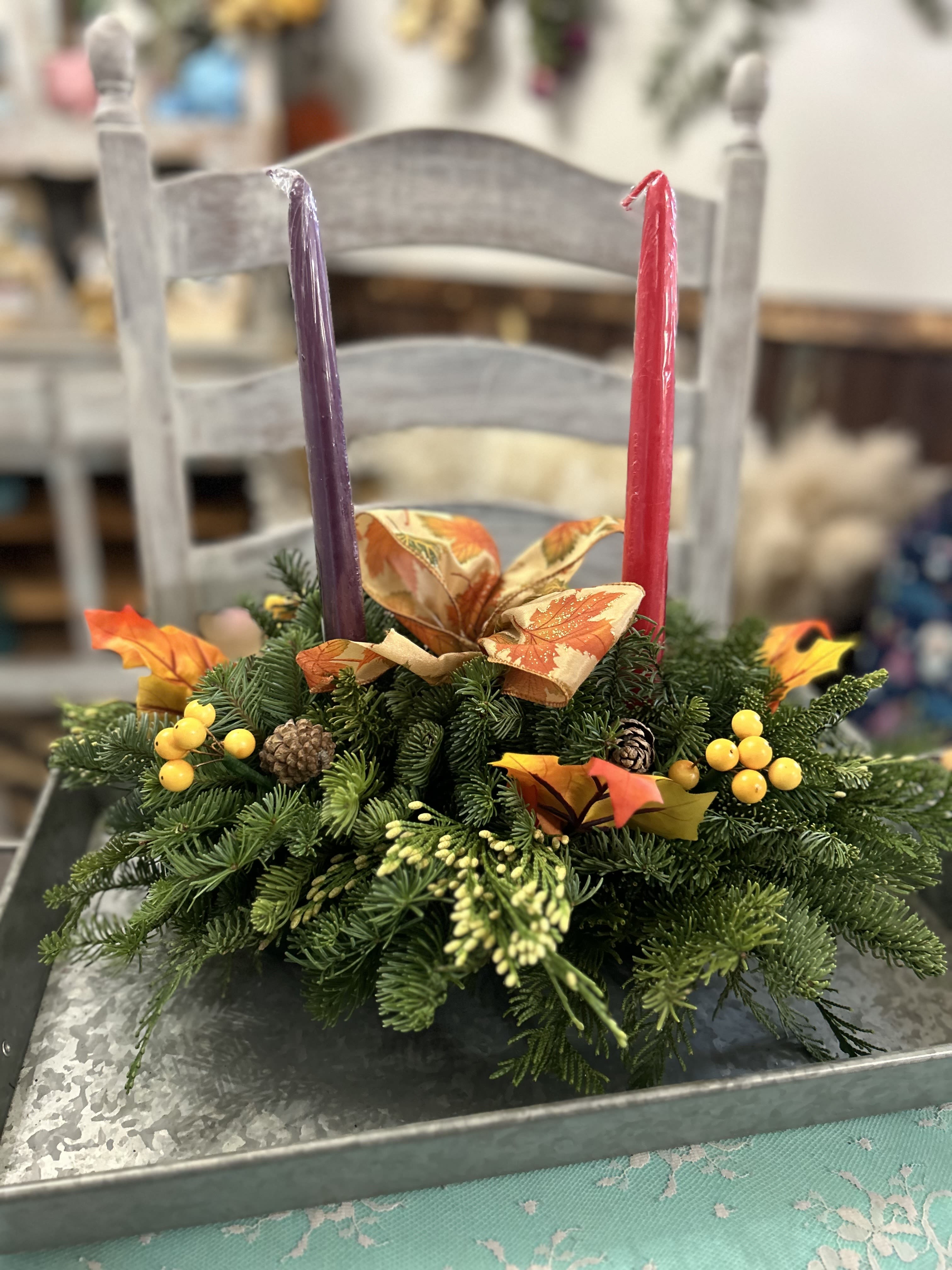 Evergreen centerpiece with fall ribbon, berries, and two taper candles on a metal tray