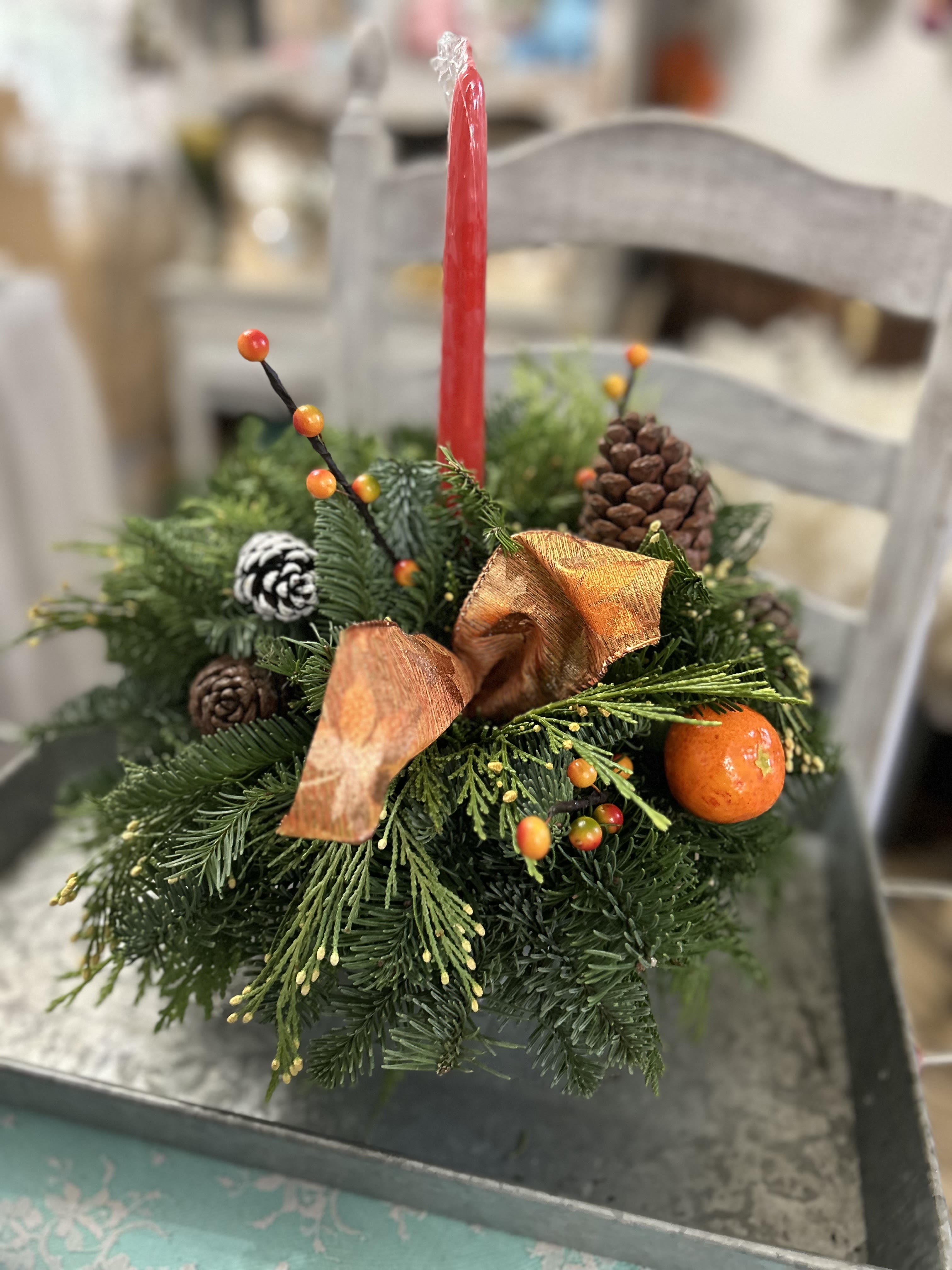 Evergreen centerpiece with red taper candle, pinecones, ribbon, berries, and an orange accent.