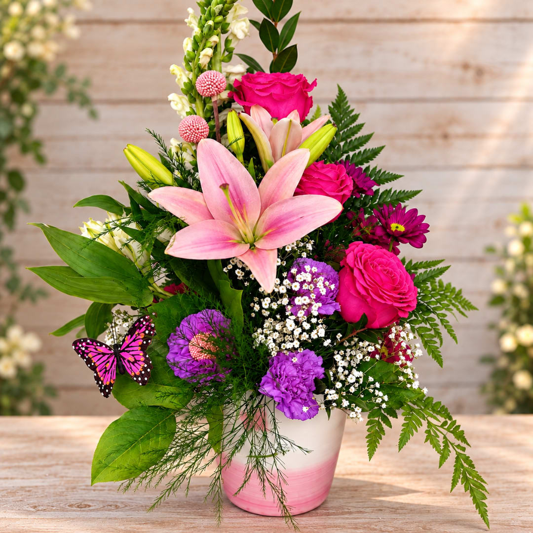 Pink lilies and roses in a white-and-pink vase with a butterfly accent