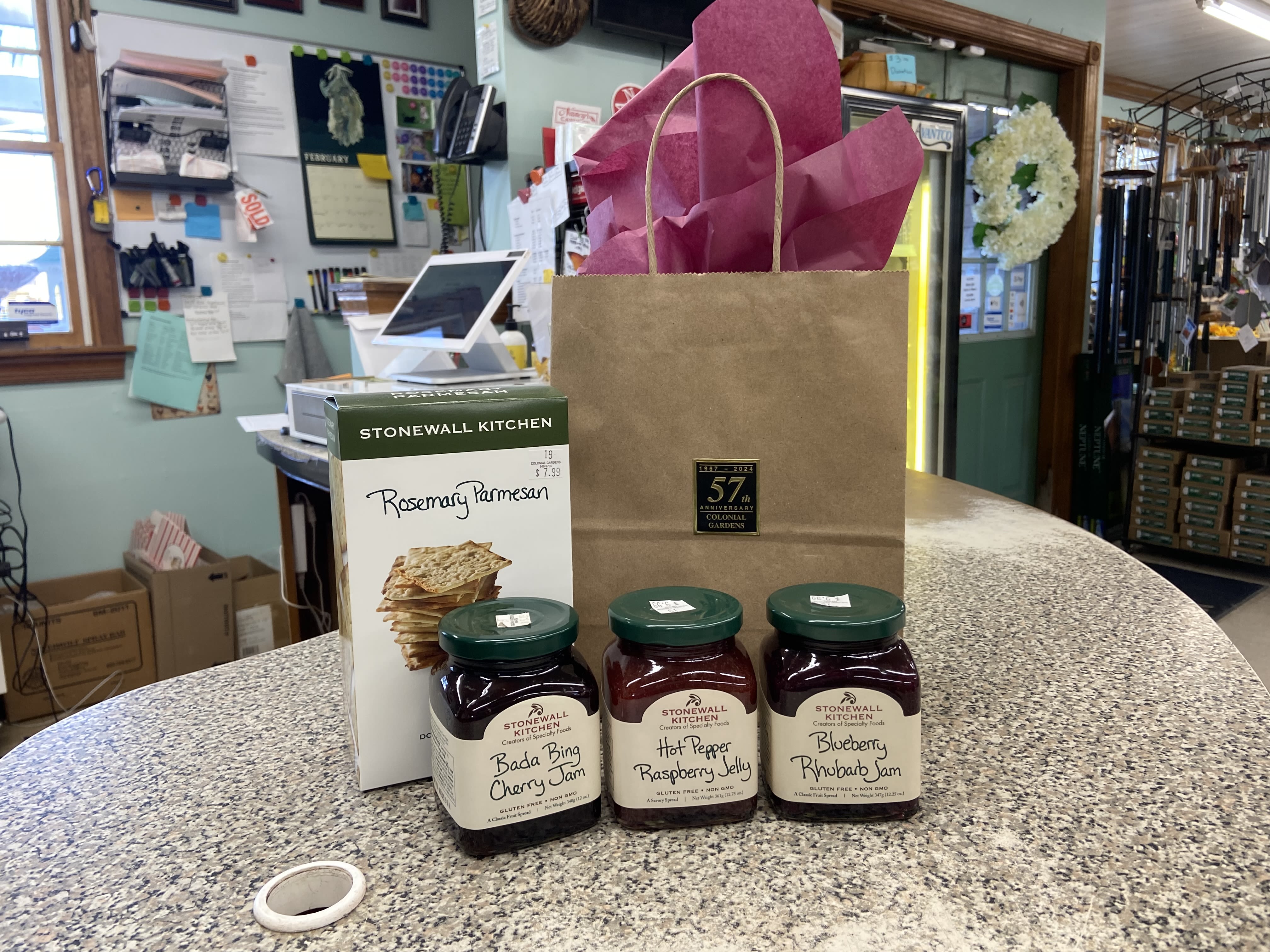 Gift bag with tissue paper, crackers, and three jars of jam on a counter