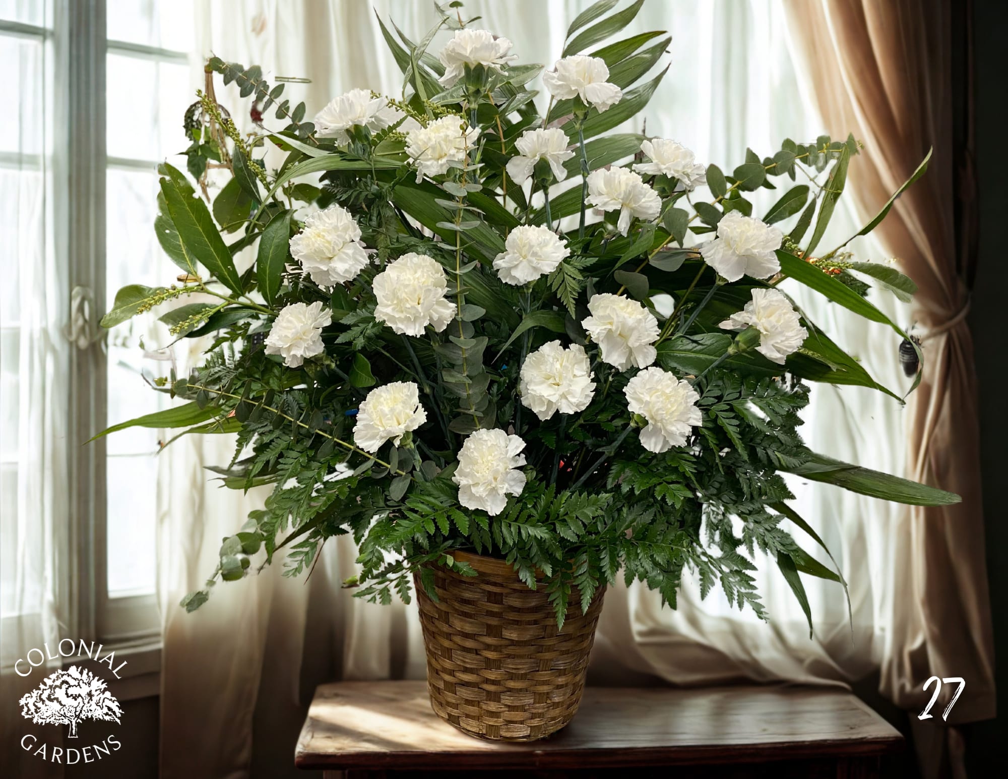 White carnations in a woven basket with mixed greenery