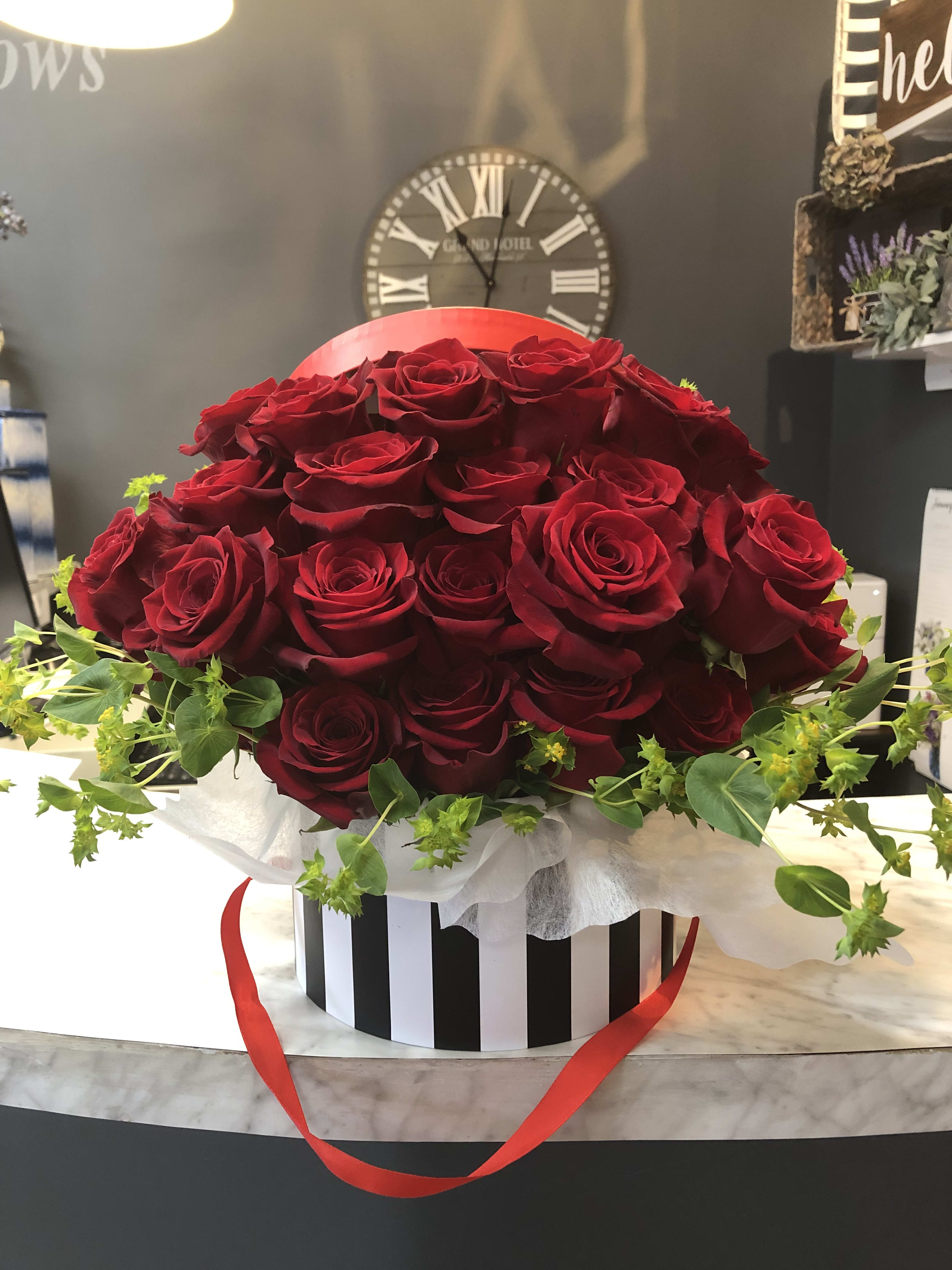 Large bouquet of red roses in a striped hatbox with a red ribbon