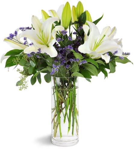 White lilies and purple filler flowers in a clear glass vase