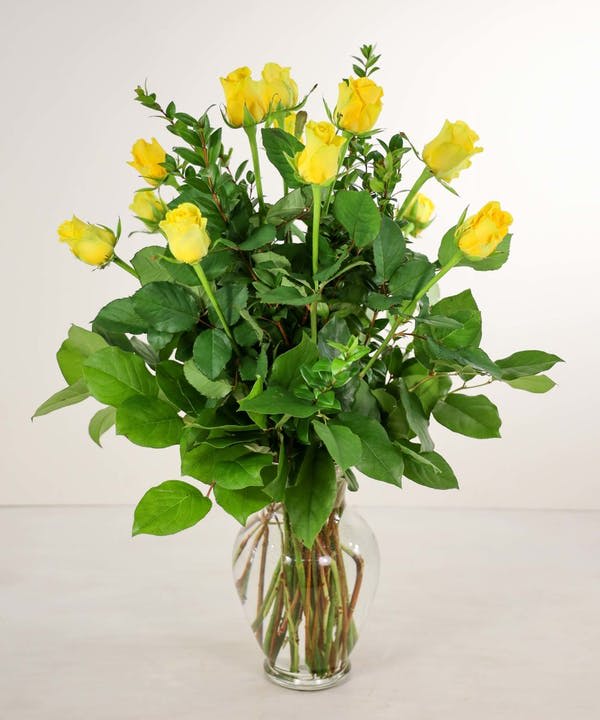 Yellow roses in a clear glass vase with dense green foliage