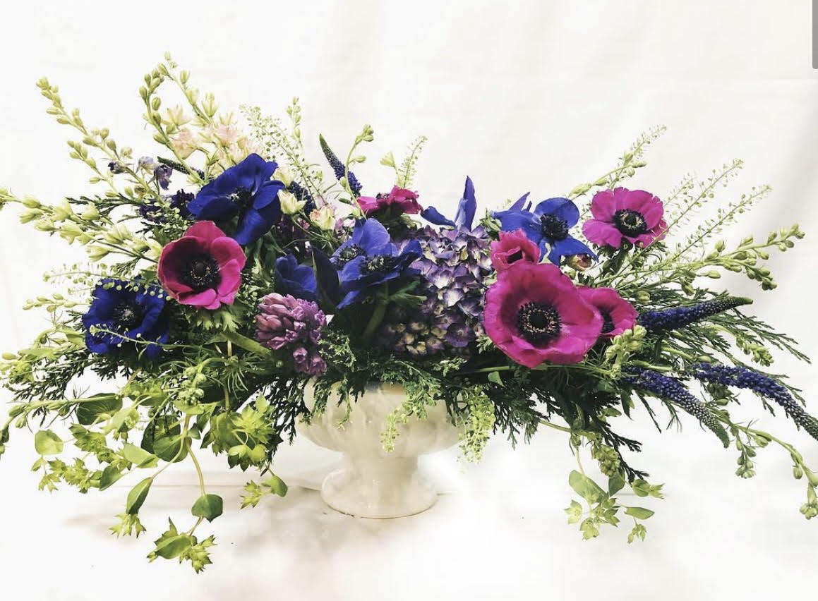 Long floral centerpiece with blue and magenta blooms in a white pedestal vase