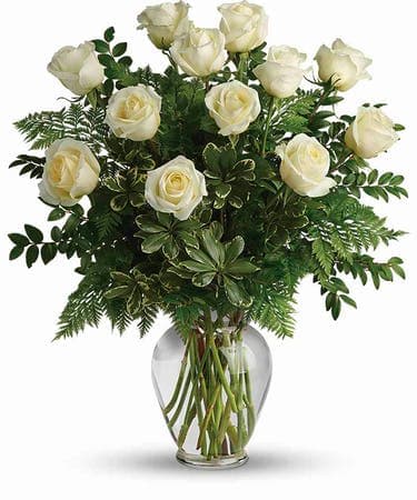 White roses arranged in a clear glass vase with lush greenery