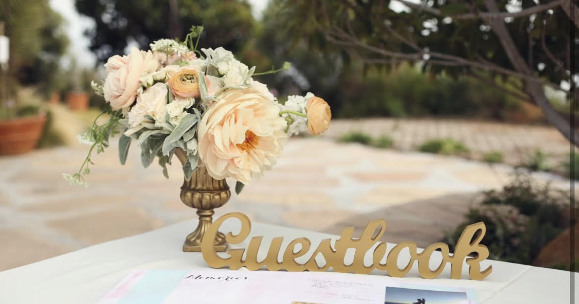 Peach and cream floral arrangement in a gold vase beside a gold guestbook sign