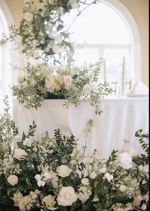 White floral arrangements with greenery on a draped table in a bright room
