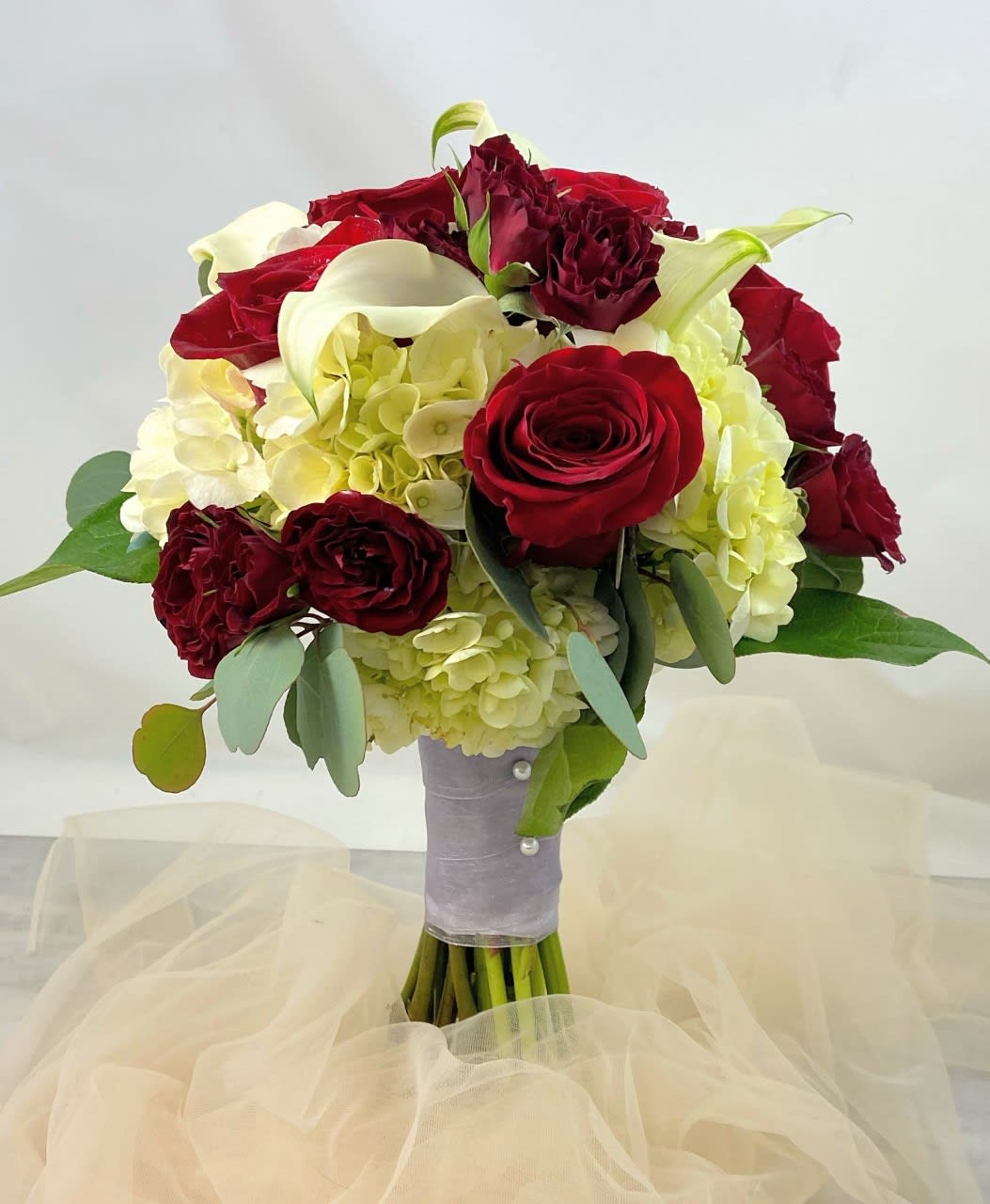 Bouquet of red roses, white calla lilies, and pale hydrangeas