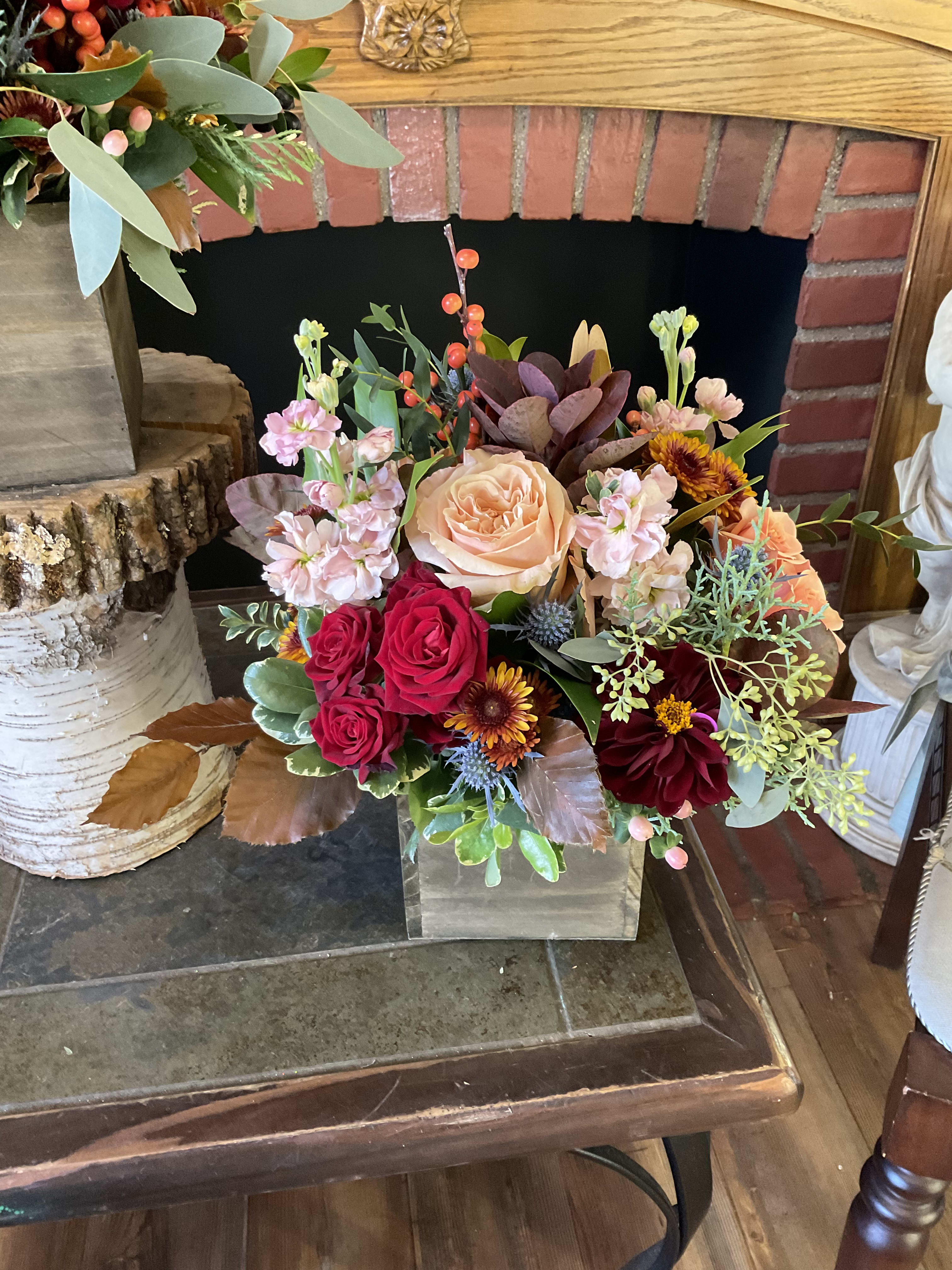 Mixed bouquet in a clear square vase with peach, red, and burgundy blooms