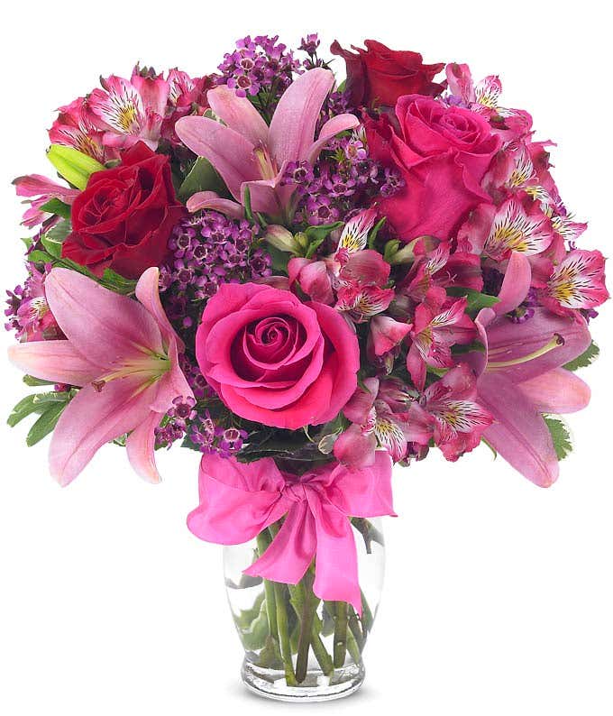 Pink and red mixed bouquet in a clear glass vase with a pink ribbon