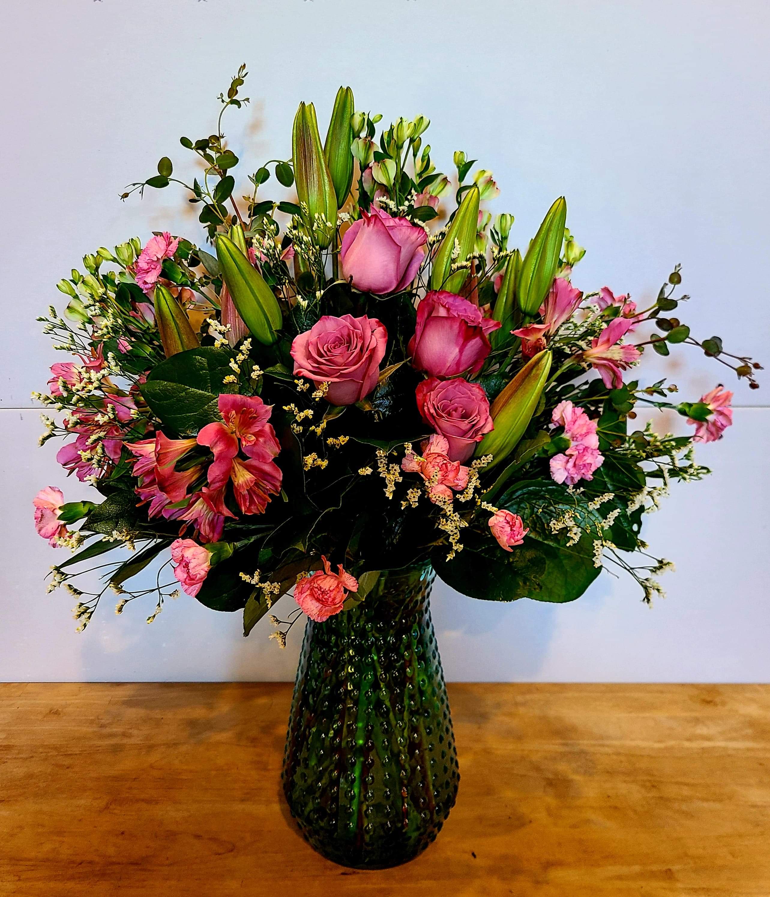 Pink roses and lilies arranged in a green glass vase