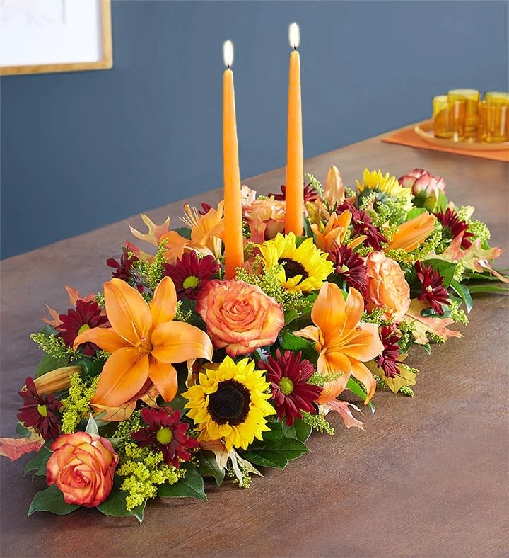 Low floral centerpiece with orange lilies, roses, sunflowers, and two orange taper candles
