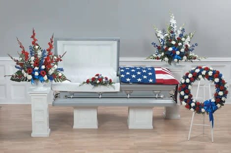 American's Pride - This package includes 4 funeral arrangements for one great price as shown. Design using Roses, Carnations, Gladiolus, Belladonna Delphinium, Gerbera Daisies, Stocks, filler, and greenery.    Package includes:  One Large Pedestal Arrangement – Design in white urn (Approximately Height 41” &amp; Width 42”) One Small Pedestal Arrangement – Design in white urn (Approximately Height 36” &amp; Width 36”) One Wreath Standing Spray (Approximately Height 49” &amp; Width 30”) One LID Decoration (Approximately Height 6” &amp; Width 28”)  Note: All selections shown are representative of the arrangements that we can prepare for you, however due to flower availability and seasonal variations we may not be able to fill your order exactly as illustrated. Your order will be filled to the specified amount with products of an equal or greater value.  Please note: Exact delivery times during the day are not possible. You may request a specific time, such as morning or afternoon, we'll try to meet the request, but we cannot guarantee it since some communities have deliveries only once a day.