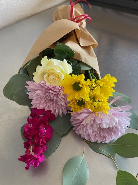 Bouquet of roses, chrysanthemums, and purple blooms wrapped in kraft paper