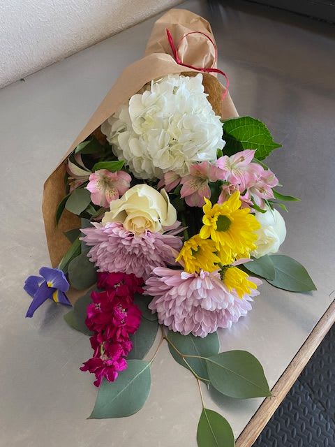 Mixed bouquet of white, pink, yellow, and purple flowers wrapped in brown paper