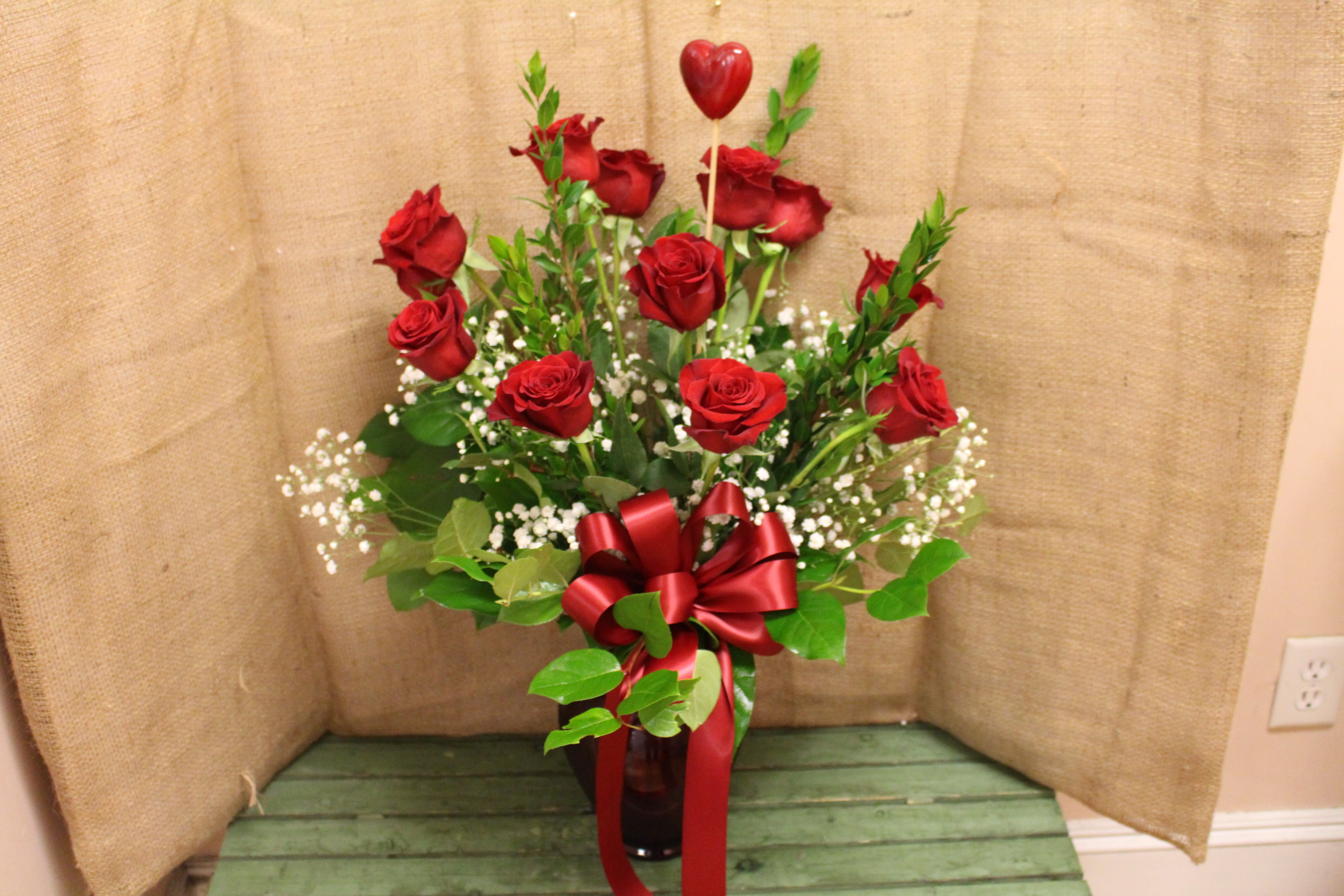Red roses in a glass vase with a red ribbon and heart pick