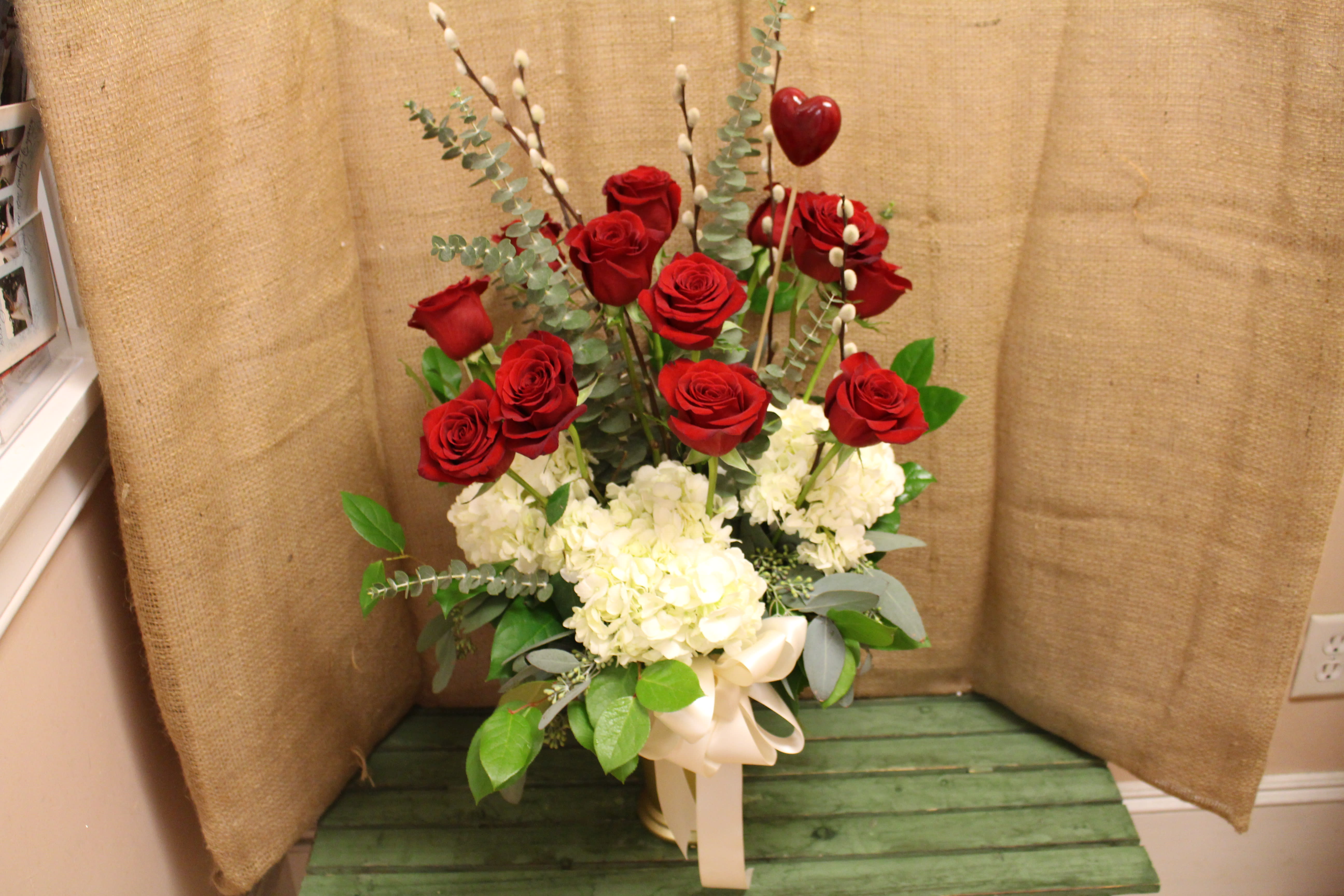 Red roses and white hydrangeas in a tall arrangement with a ribbon bow