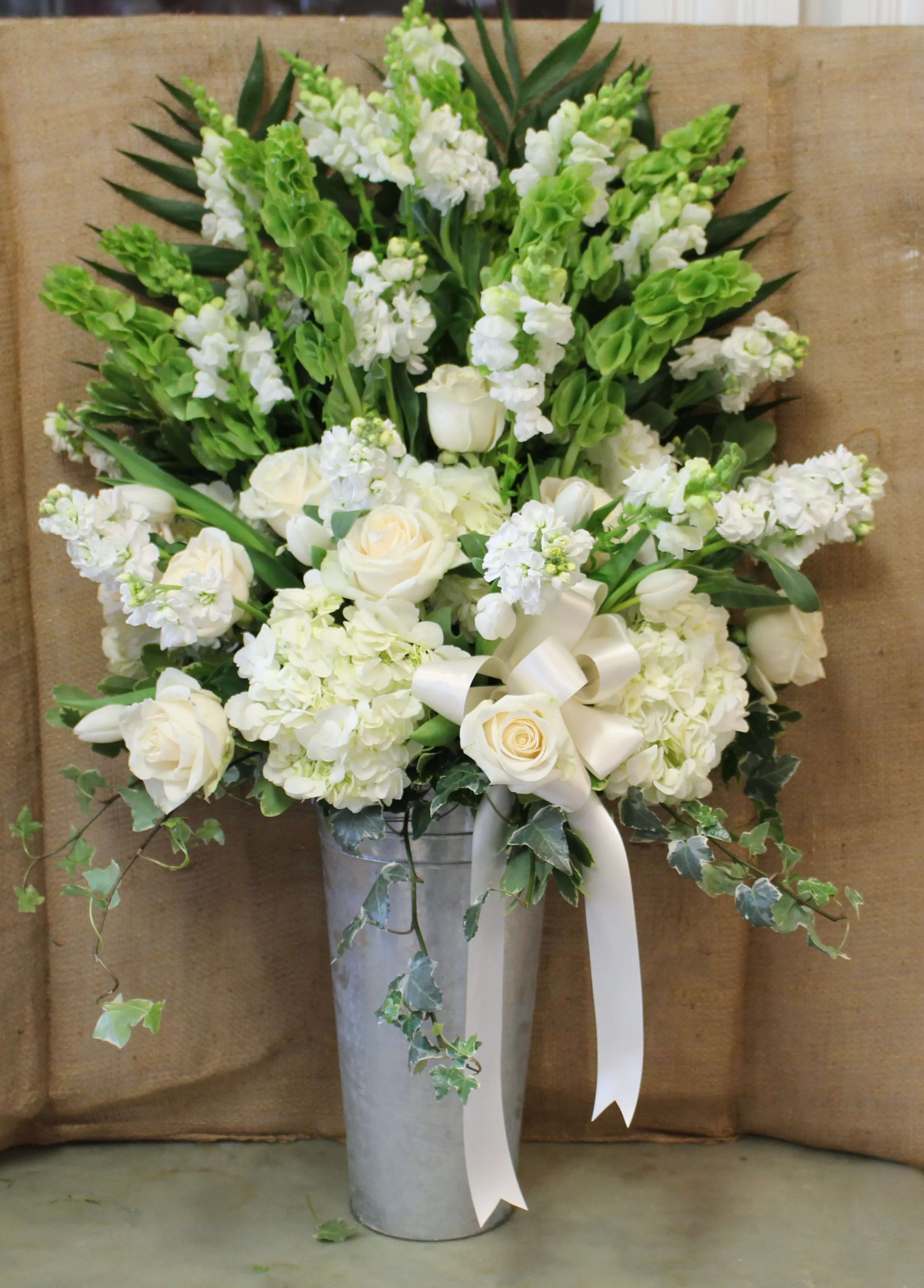 White roses and hydrangeas in a tall silver vase with a ribbon