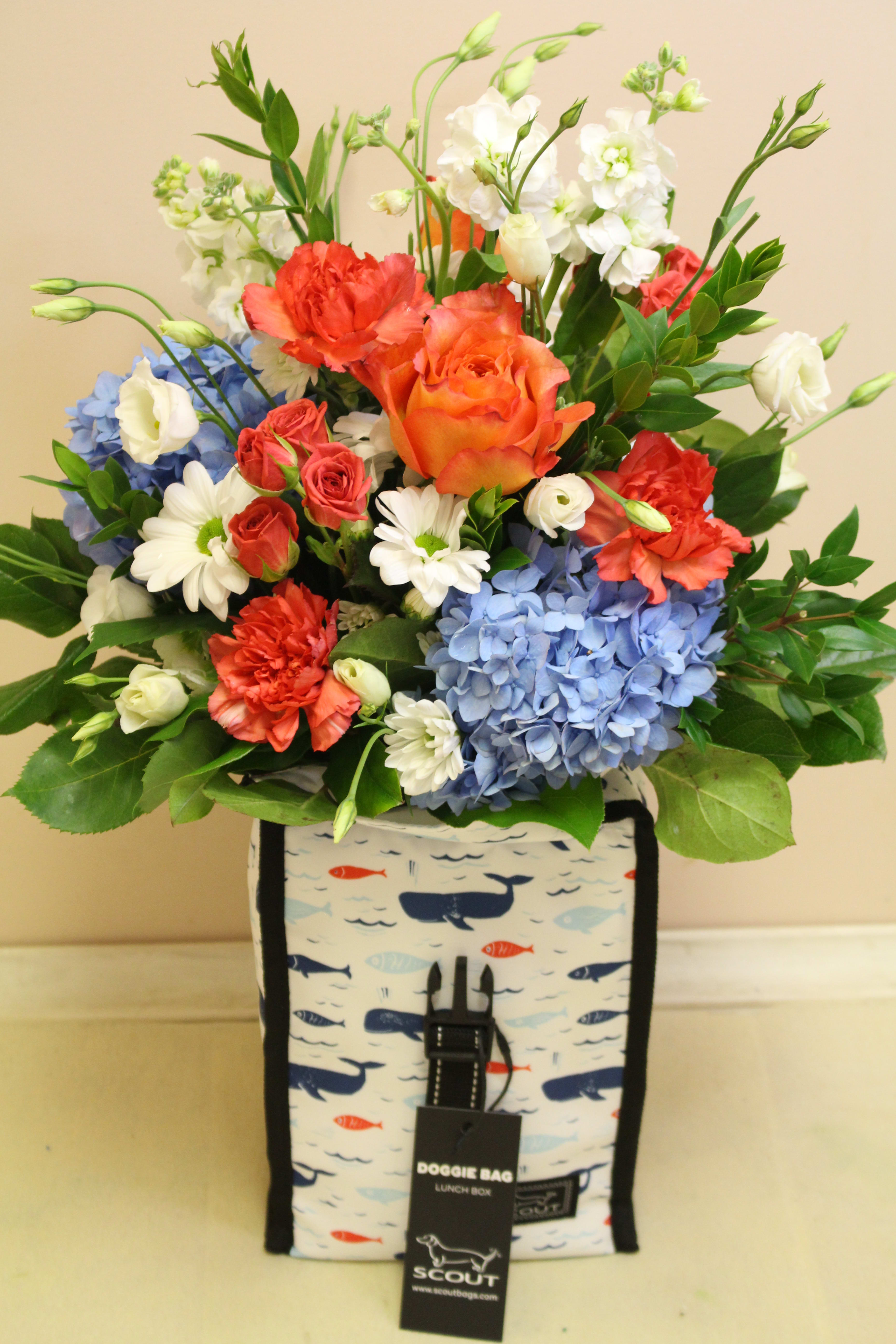 Mixed bouquet of roses, carnations, hydrangeas, and daisies in a patterned lunch bag