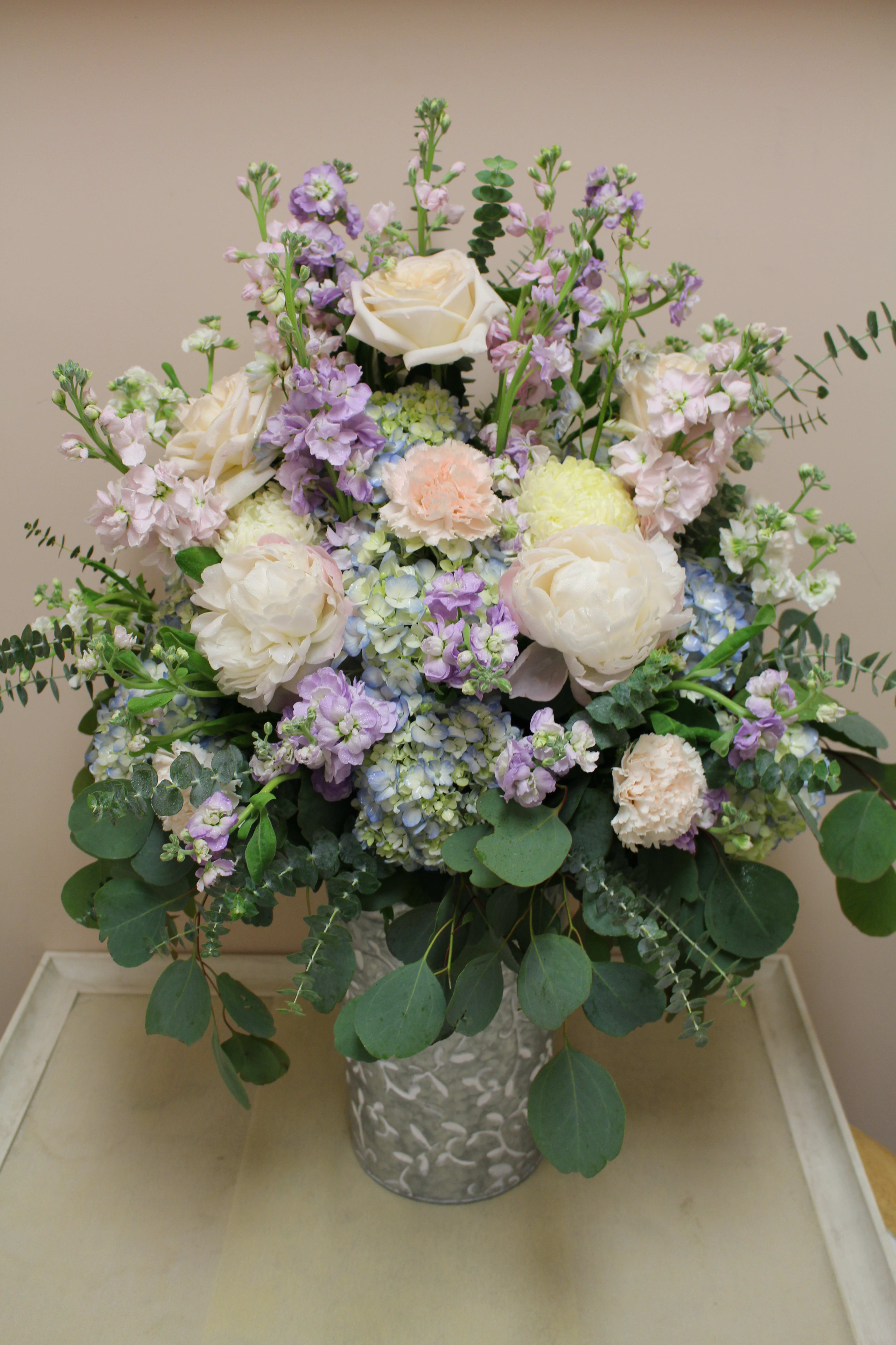 Pastel bouquet of white roses, hydrangeas, and lavender blooms in a metal vase