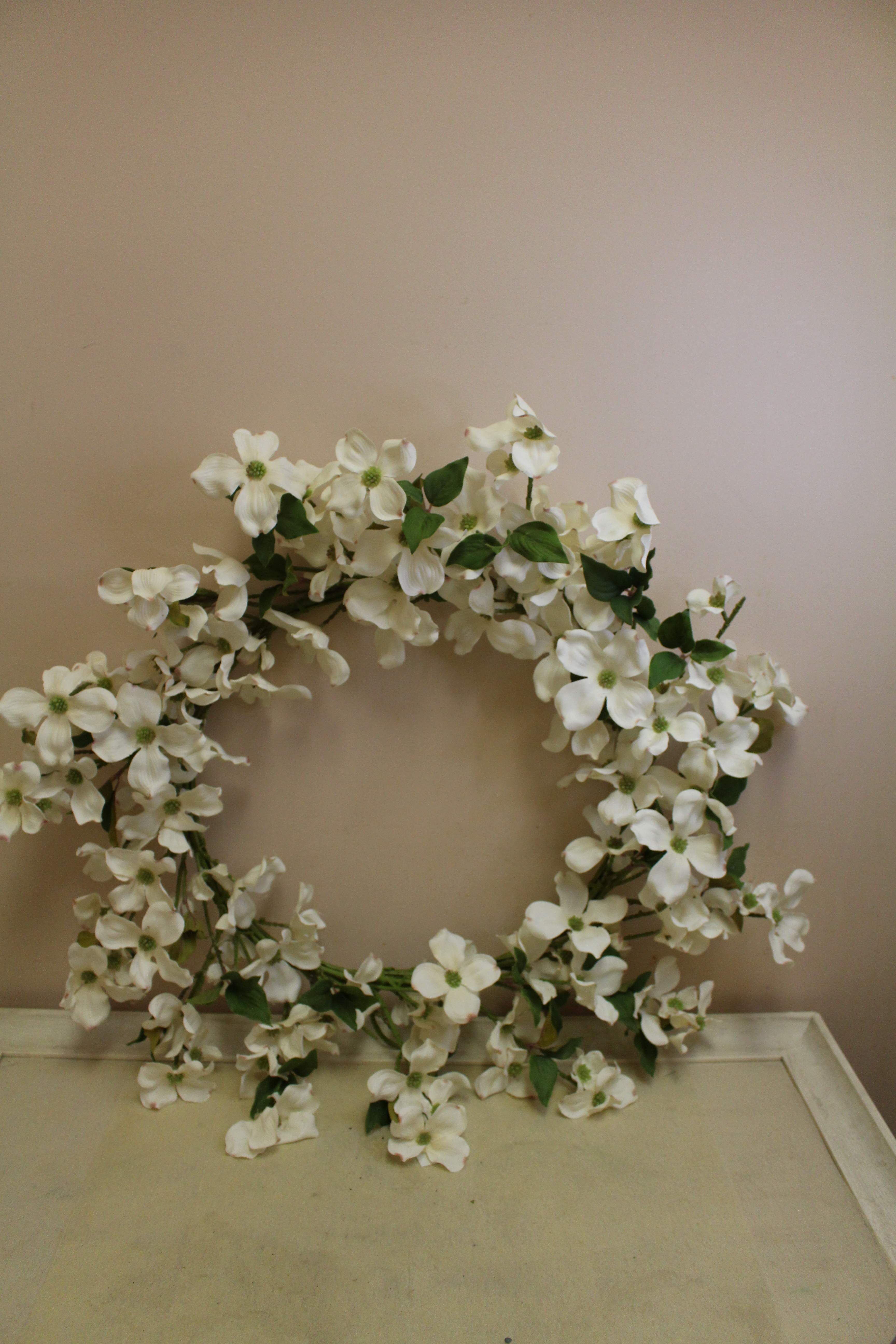 White floral wreath with green leaves on a neutral wall