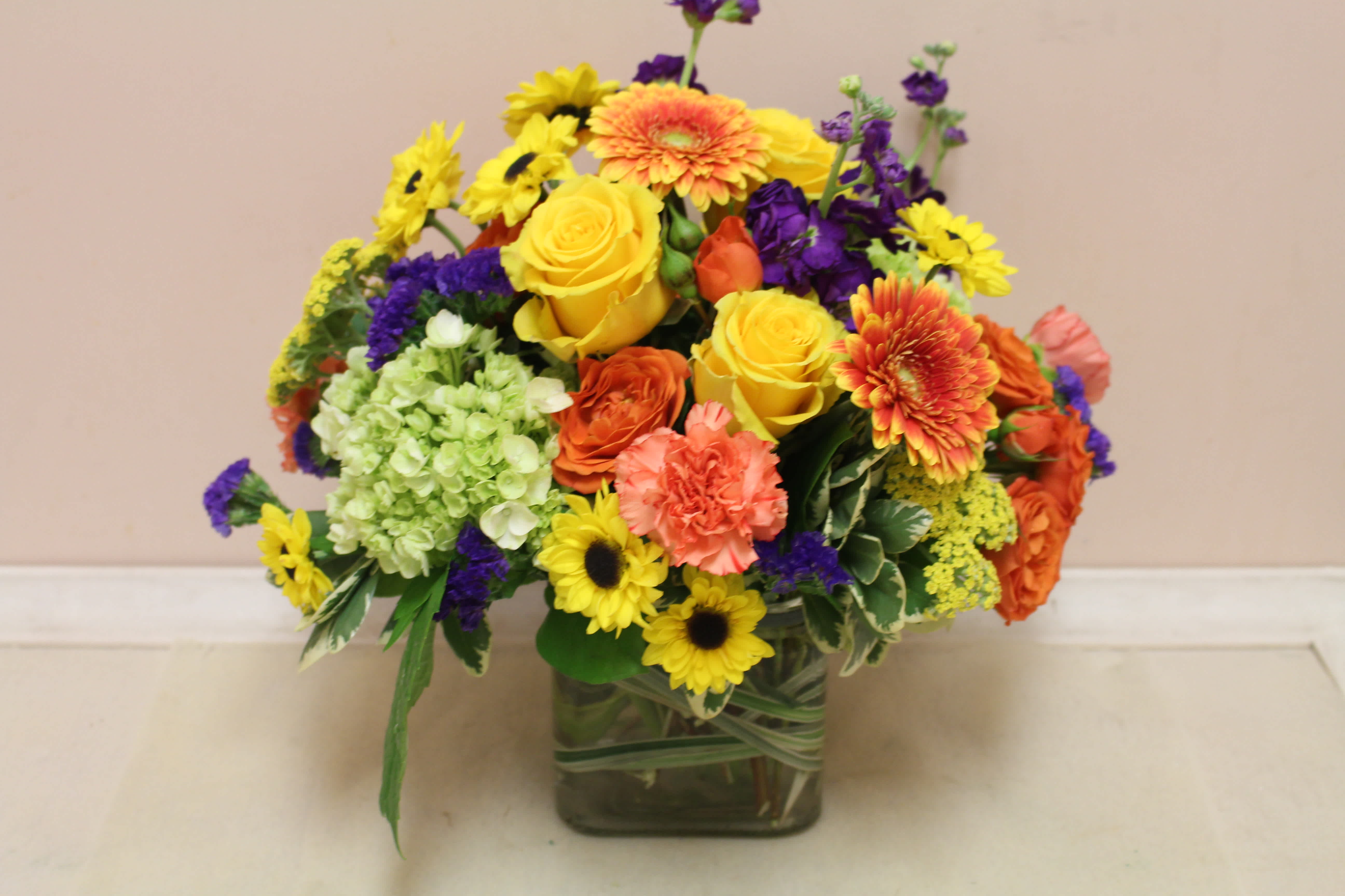 Mixed bouquet of yellow, orange, purple, and green flowers in a square glass vase